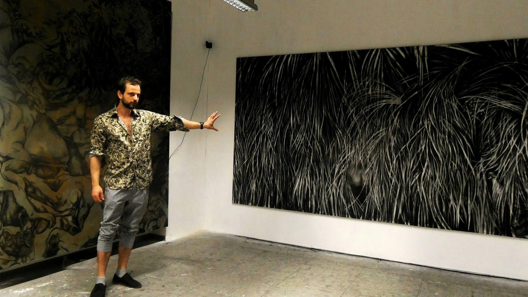 Ein junger Mann steht vor zwei düster wirkenden, großen Bildern.