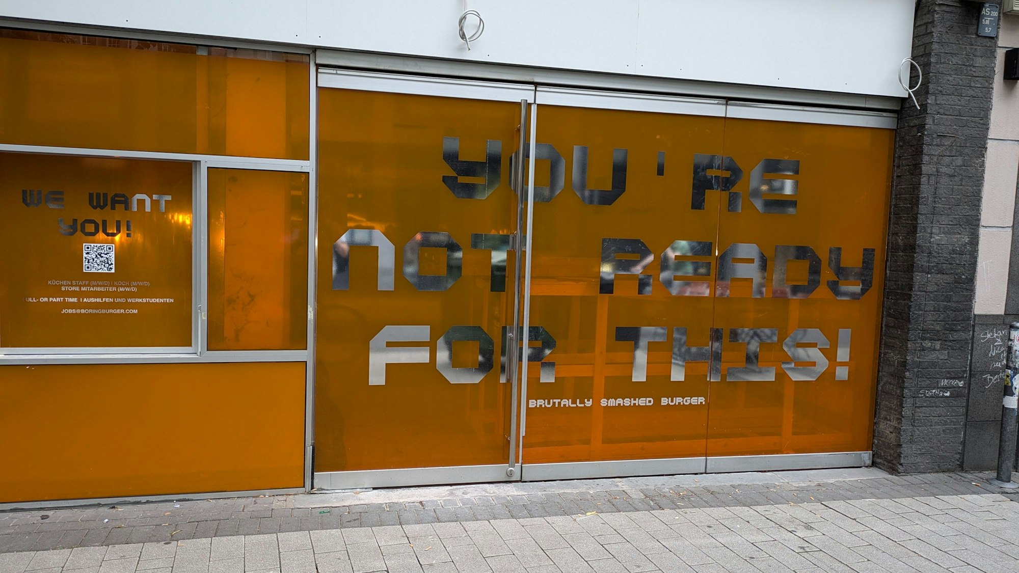Die Ladenfront ist mit einer leuchtend-orangen Folie beklebt, auf der steht „you´re not ready for this“.