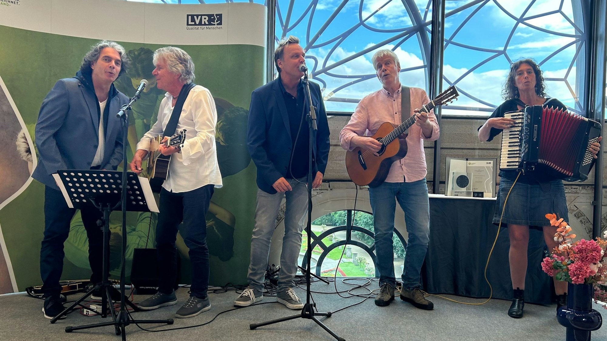 Bläck Fööss-Musiker Alex Vesper (v.l.), Bömmel Lückerath und Mirko Bäumer stehen mit Günter Schwanenberg und Tanja Krämer auf einer Bühne im Dachsalon der Flora.