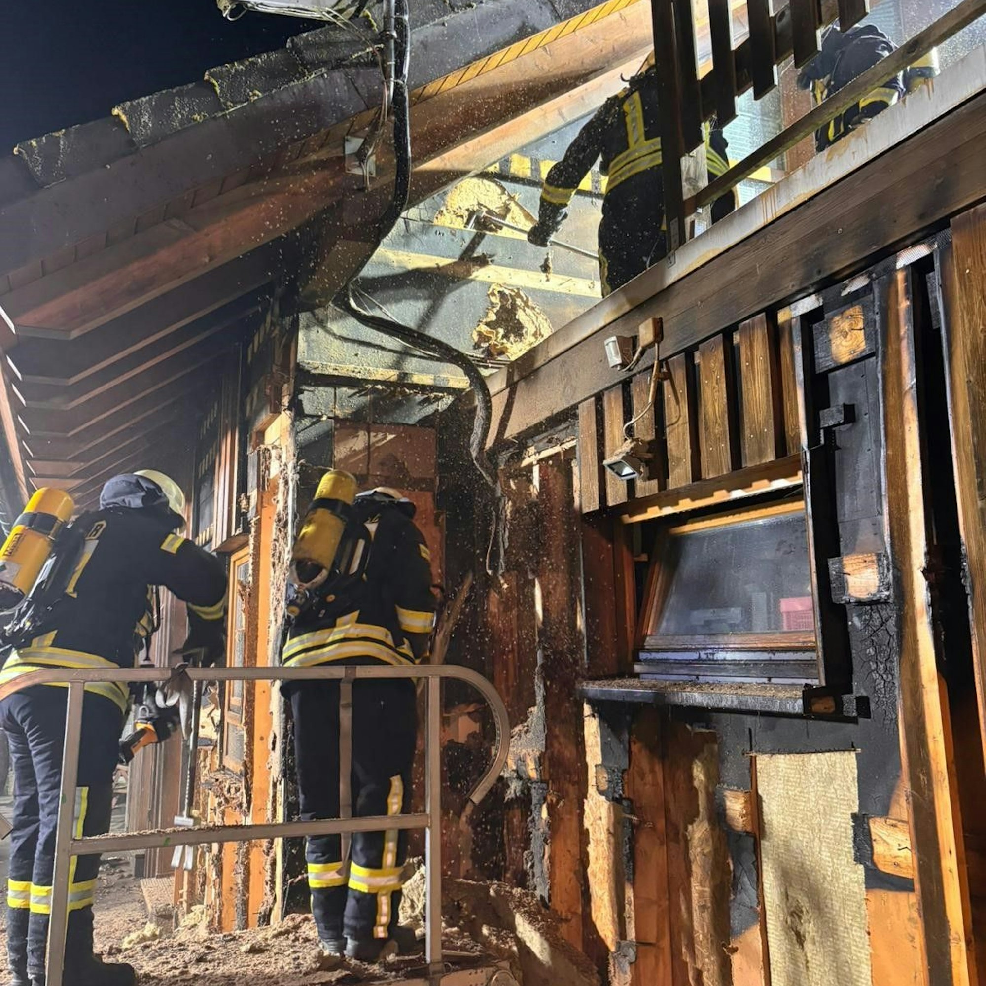 Feuerwehrleute arbeiten unter Atemschutz an einem Haus in Blankenheim-Mülheim. Sie haben die hölzerne Fassade geöffnet, zahlreiche schwarz verkohlte Stellen sind zu erkennen.
