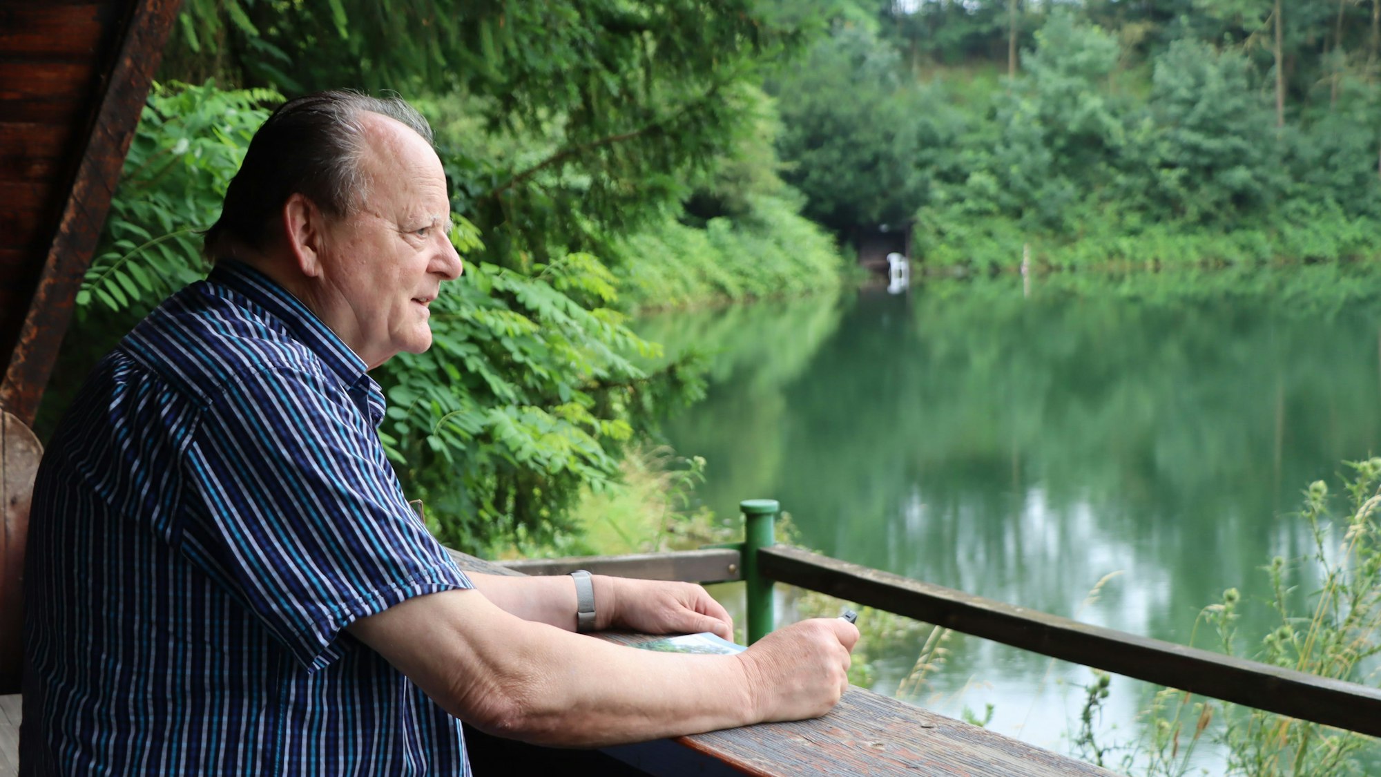 Ein Mann steht an einem See und blickt auf das Wasser.