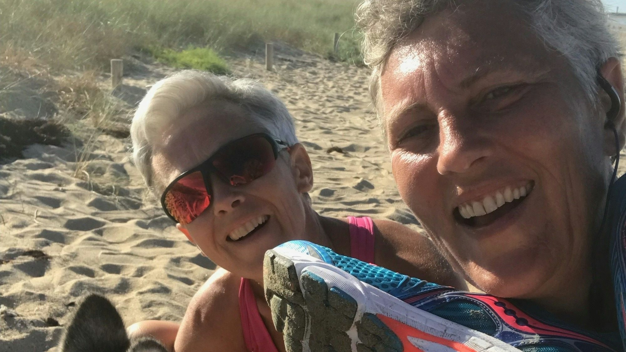 Zwei Frauen sitzen mit einem Husky am Strand.