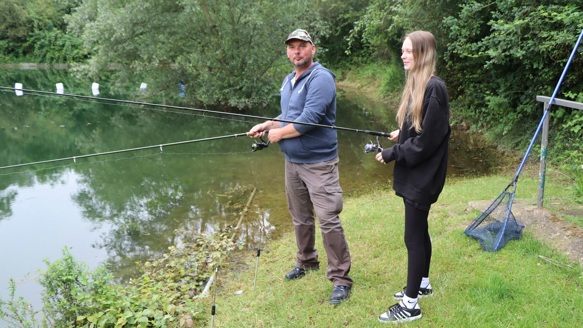 Zwei Menschen stehen an einem See und angeln.