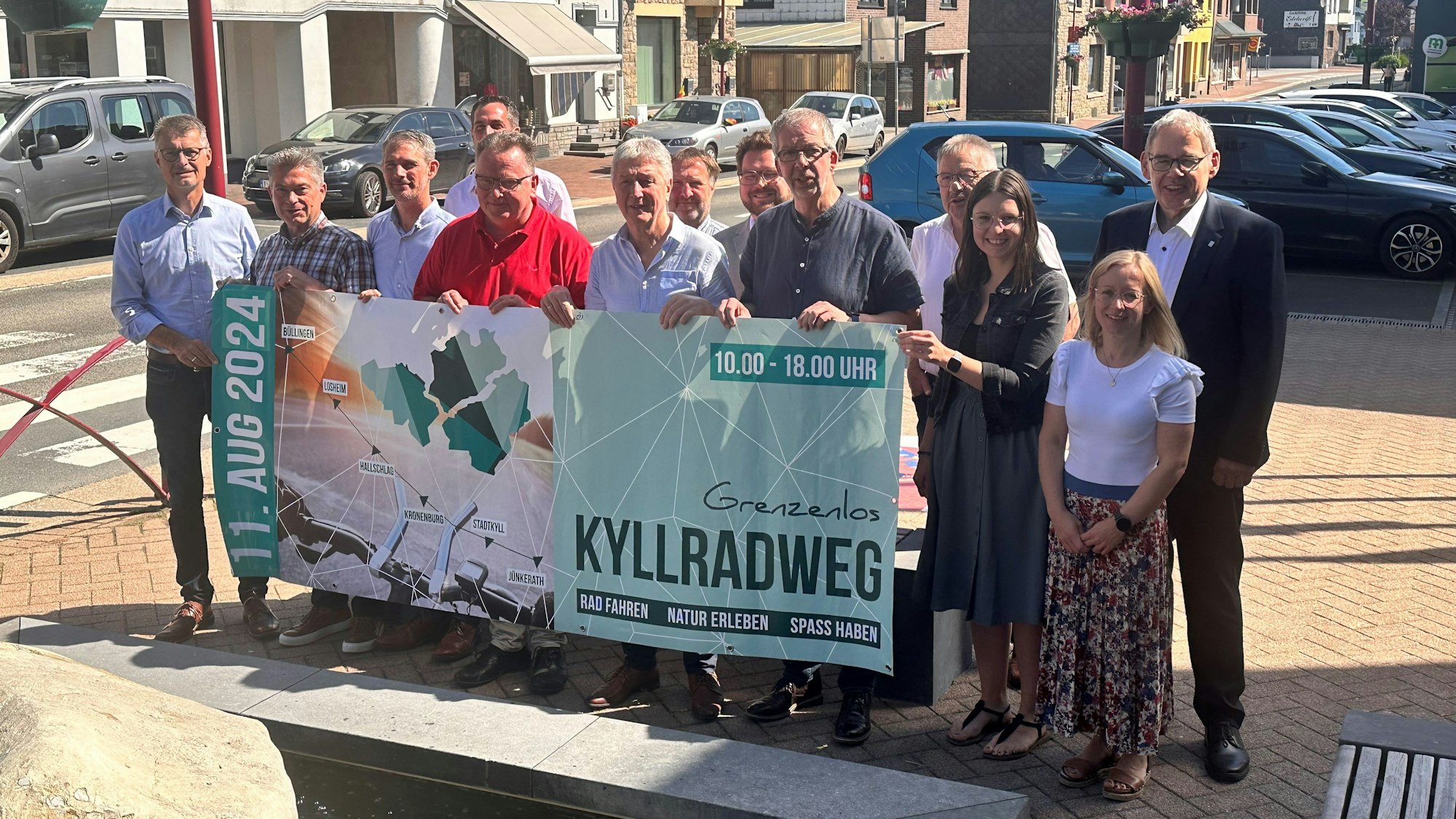 Die Organisatoren stehen in einer Reihe nebeneinander. Sie halten ein Werbebanner vor sich.