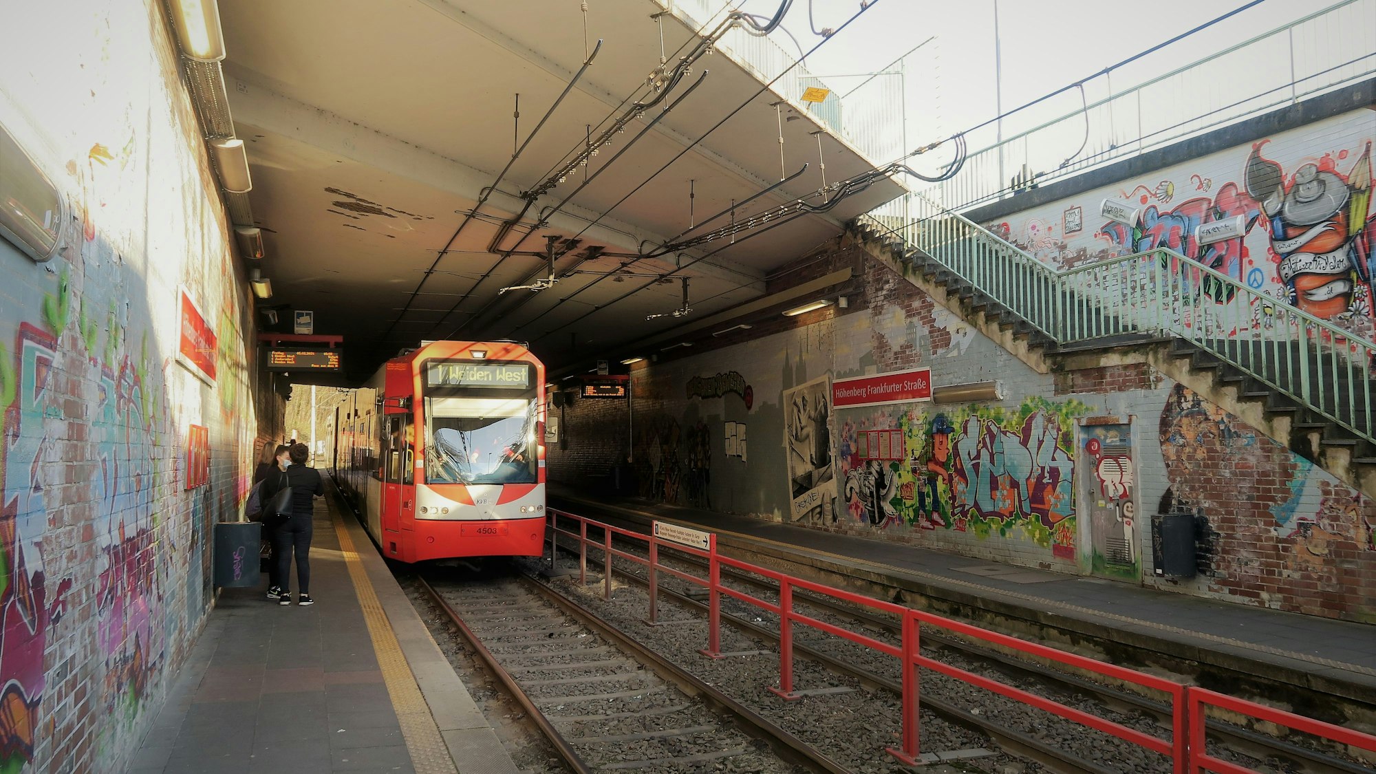 Eine Bahn der Linie 1 an einer Haltestelle, deren Wände Graffities zieren.