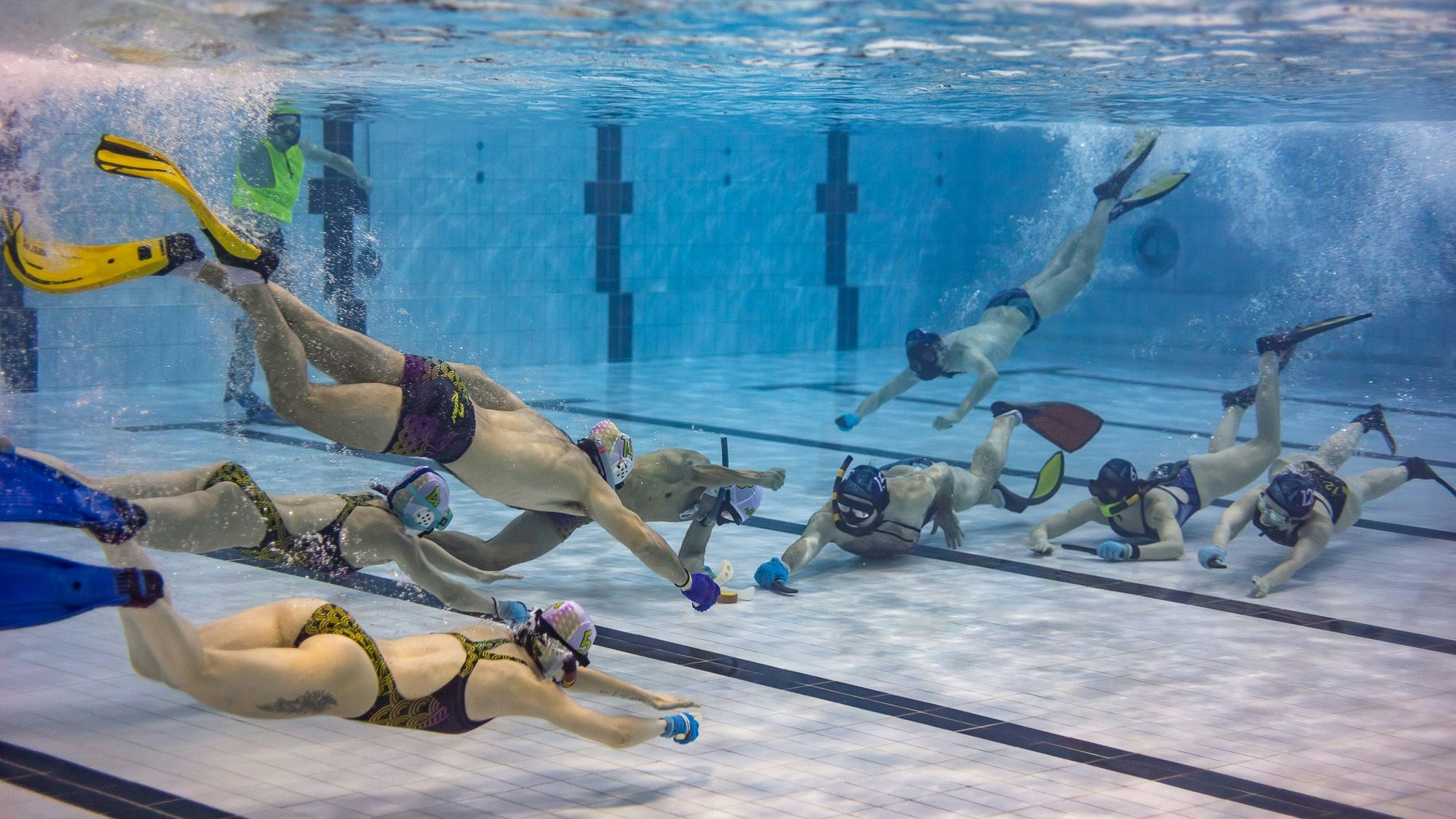 Mehrere Spieler spielen Unterwasserhockey in einem Schwimmbecken.