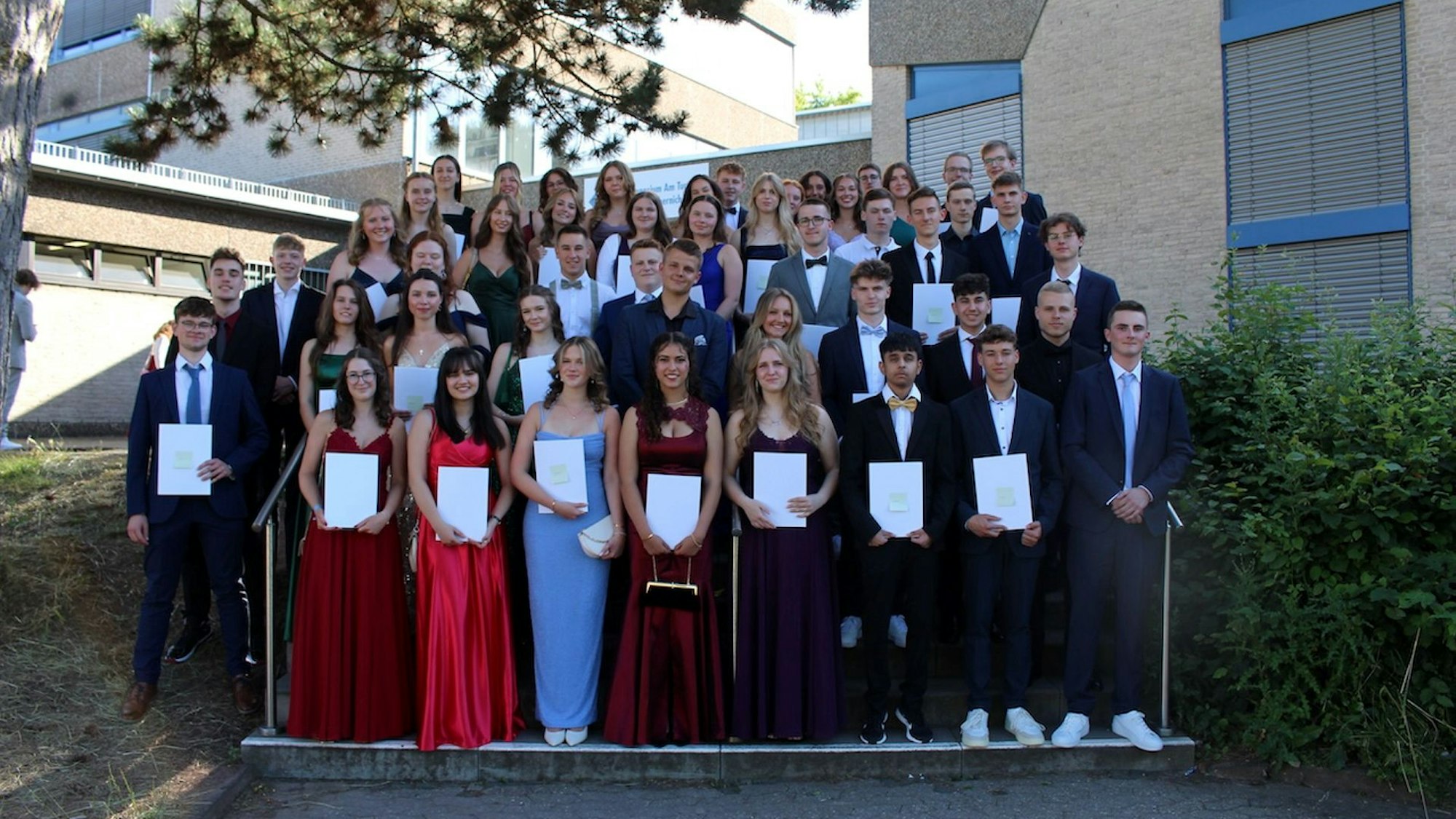 Der Abiturjahrgang steht in festlicher Garderobe auf einer Treppe vor dem Schulgebäude des Gymnasiums am Turmhof.