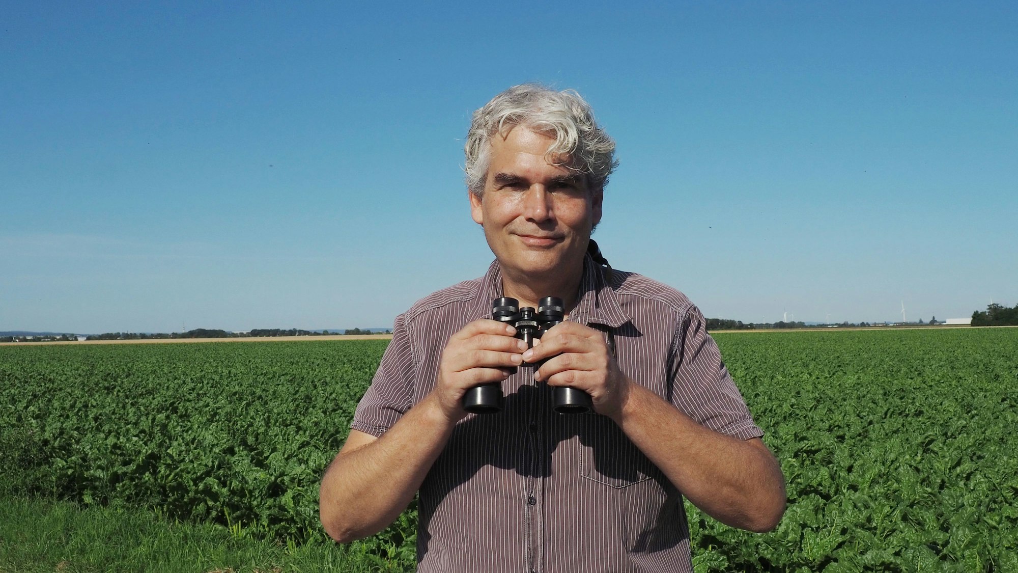 Axel Hirschfeld steht mit einem Fernglas auf einem Feld.