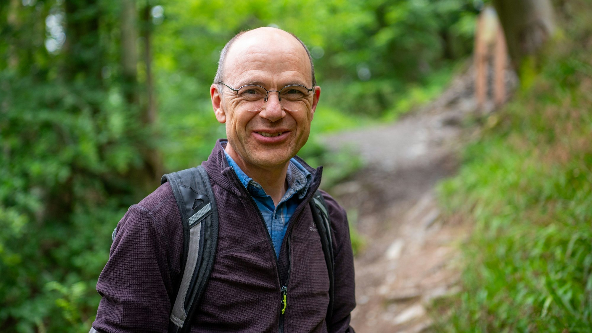 Georg Toporowsky mit lilafarbener Jacke und Rucksack bei einer Wanderung auf dem Schöpfungspfad.