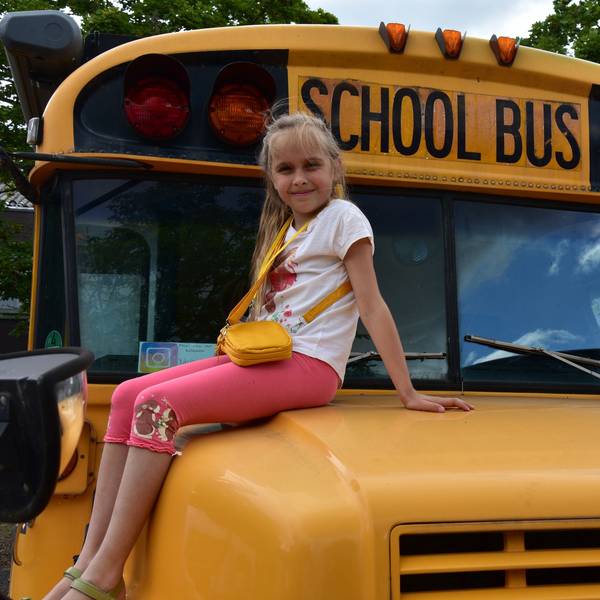Ein Mädchen sitzt auf der Motorhaube eines amerikanischen Schulbusses.