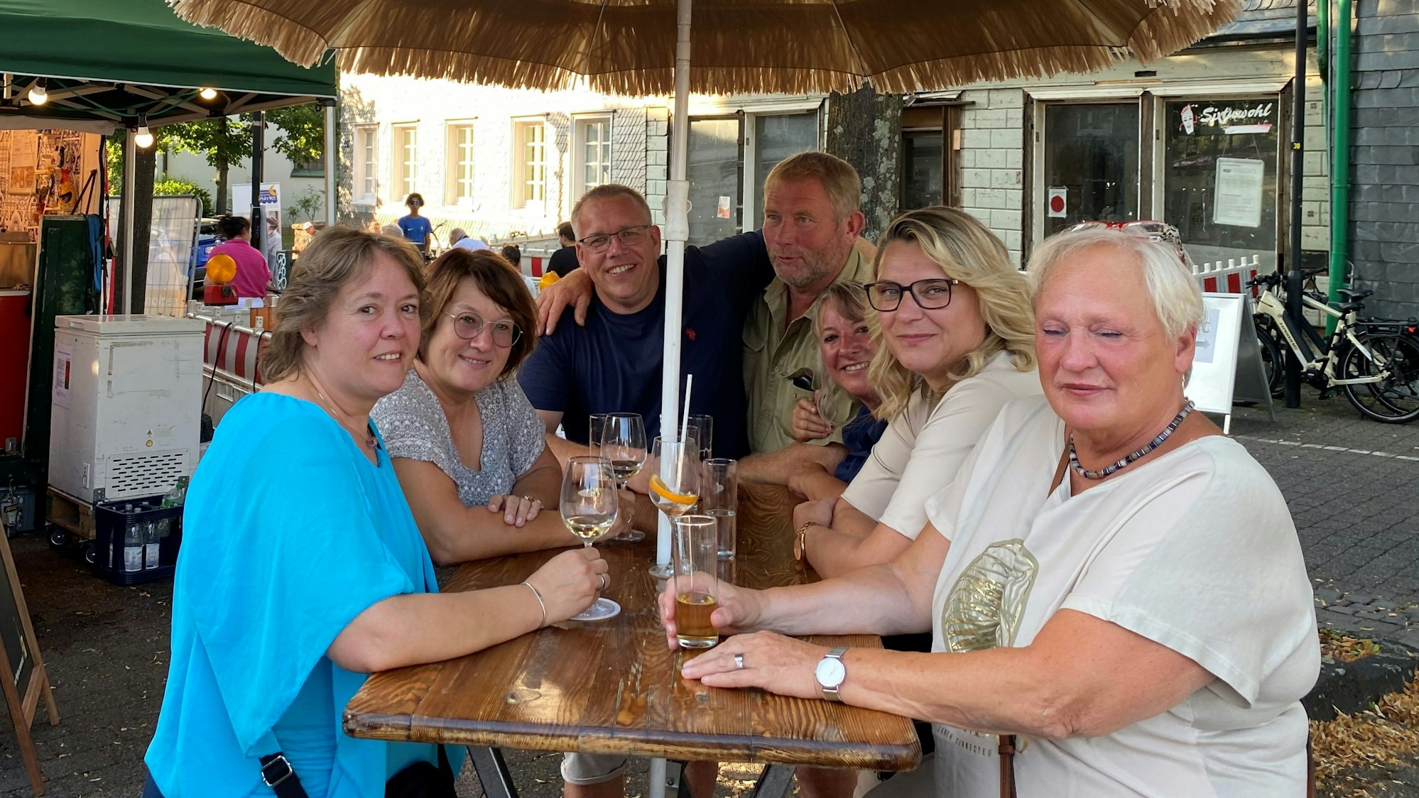 Frauen und Männer sitzen an einem Tisch auf einem Platz.