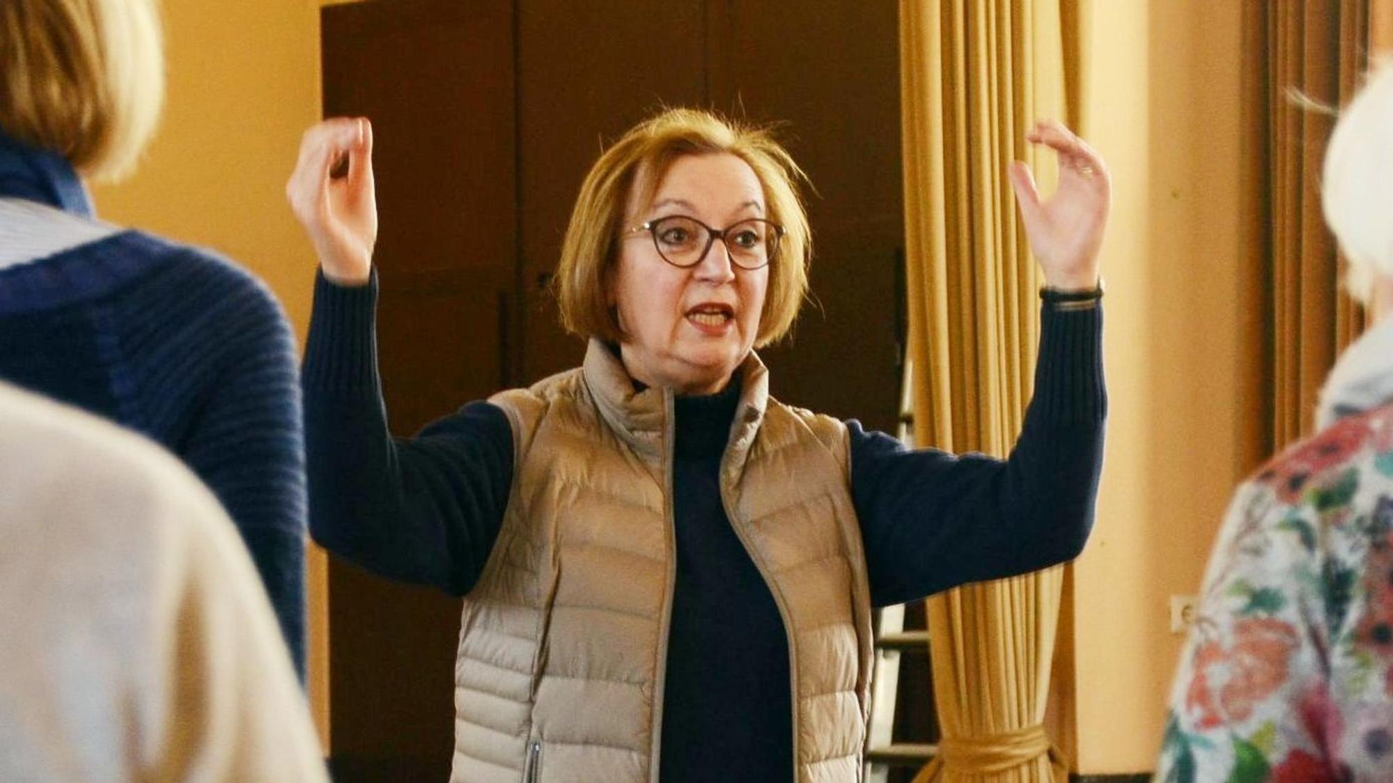 Eine Frau dirigiert einen Chor, dabei singt sie auch selbst.