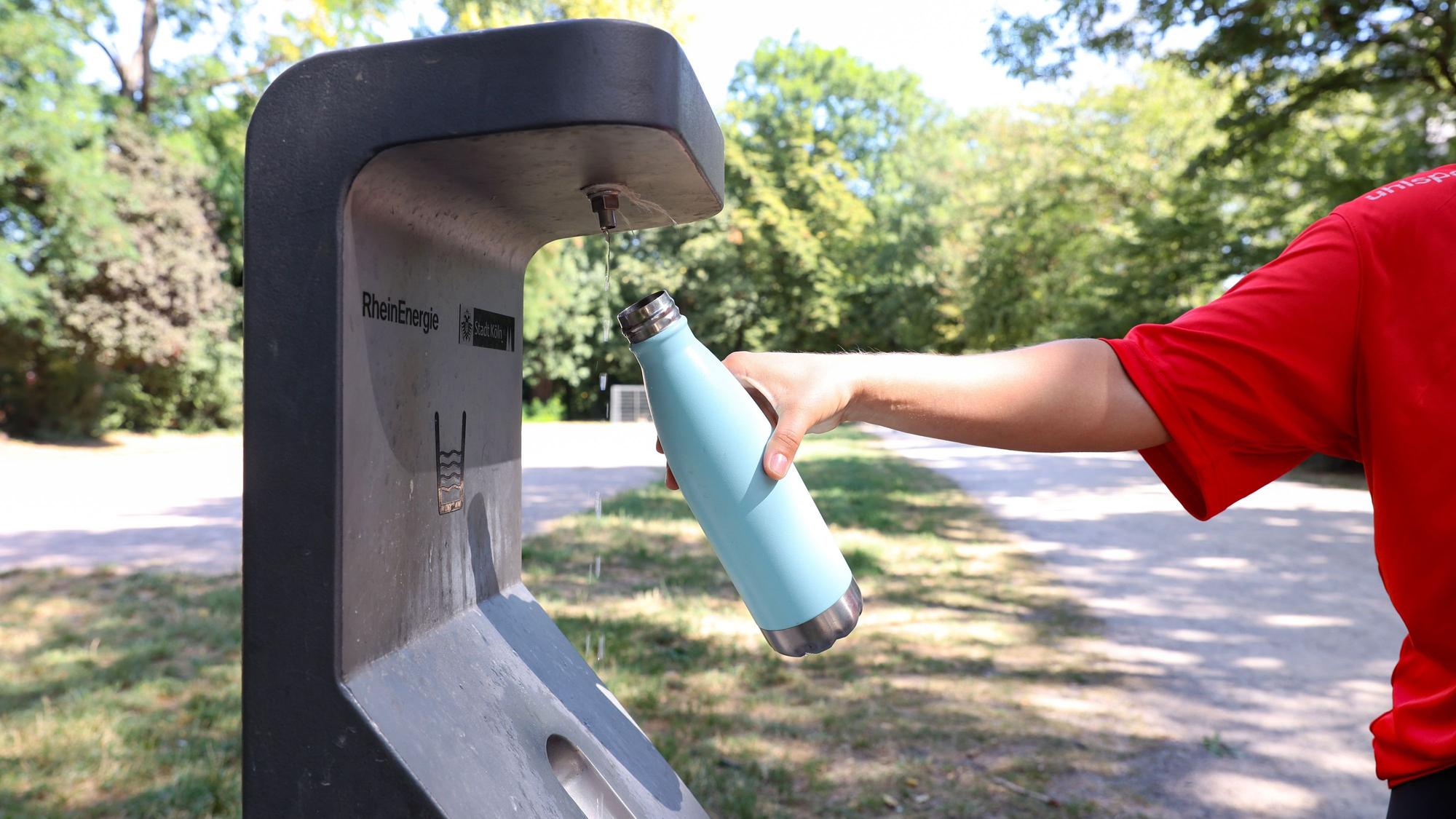 Person hält Trinkflasche unter Trinkwasserbrunnen der RheinEnergie im Takufeld. (Archivbild)