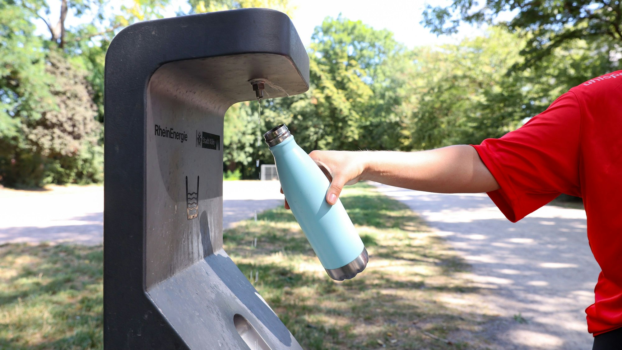 Person hält Trinkflasche unter Trinkwasserbrunnen der RheinEnergie im Takufeld. (Archivbild)