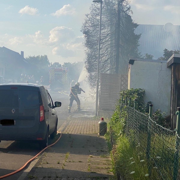 Ein Feuerwehrmann löscht einen Brand an einer Hecke.