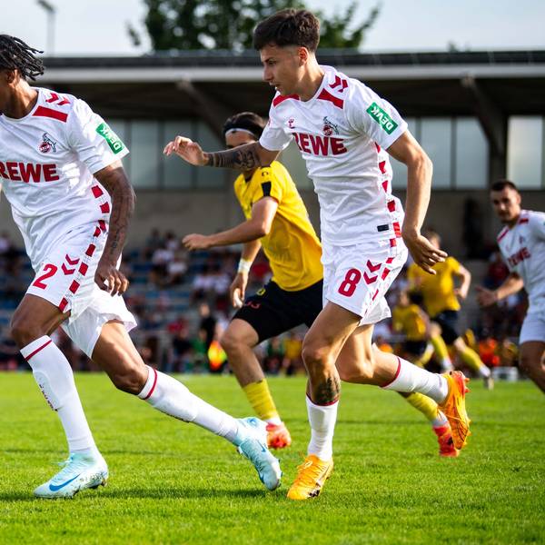 Das Bild zeigt den Fußballspieler des 1. FC Köln, Damion Downs (l.), wie er den Ball im Mittelfeld vorantreibt.