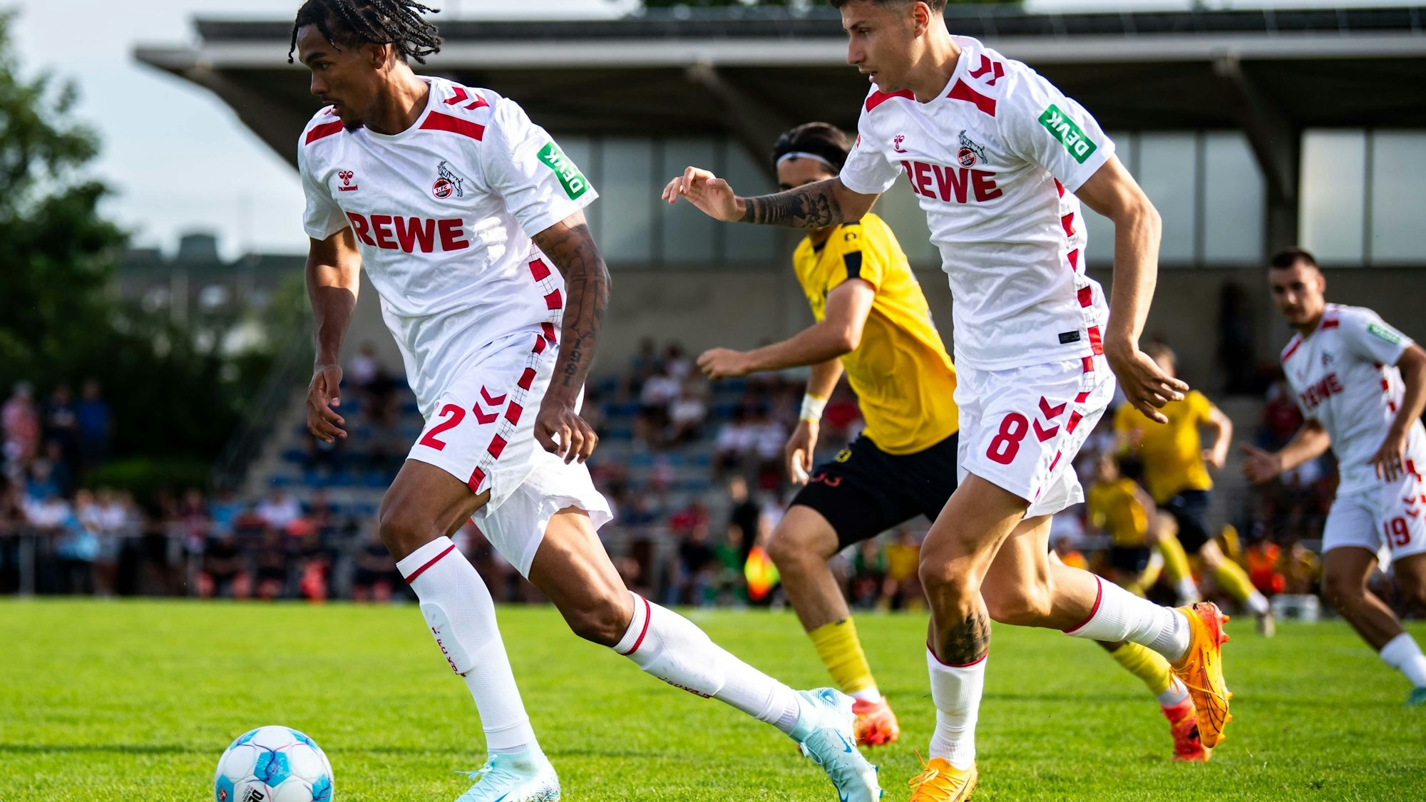 Das Bild zeigt den Fußballspieler des 1. FC Köln, Damion Downs (l.), wie er den Ball im Mittelfeld vorantreibt.
