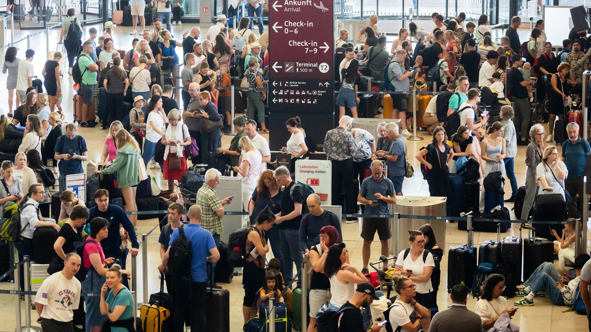 19.07.2024, Brandenburg, Schönefeld: Passagiere warten am Hauptstadtflughafen BER vor Check-in-Schaltern. Am Flughafen BER ist der Flugverkehr eingestellt worden. Als Grund dafür werden technische Probleme genannt. Foto: Christoph Soeder/dpa +++ dpa-Bildfunk +++