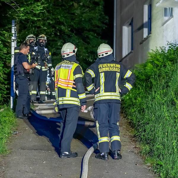 Mehrere Feuerwehrleute stehen vor einem Gebäude, in dem es gebrannt hat.