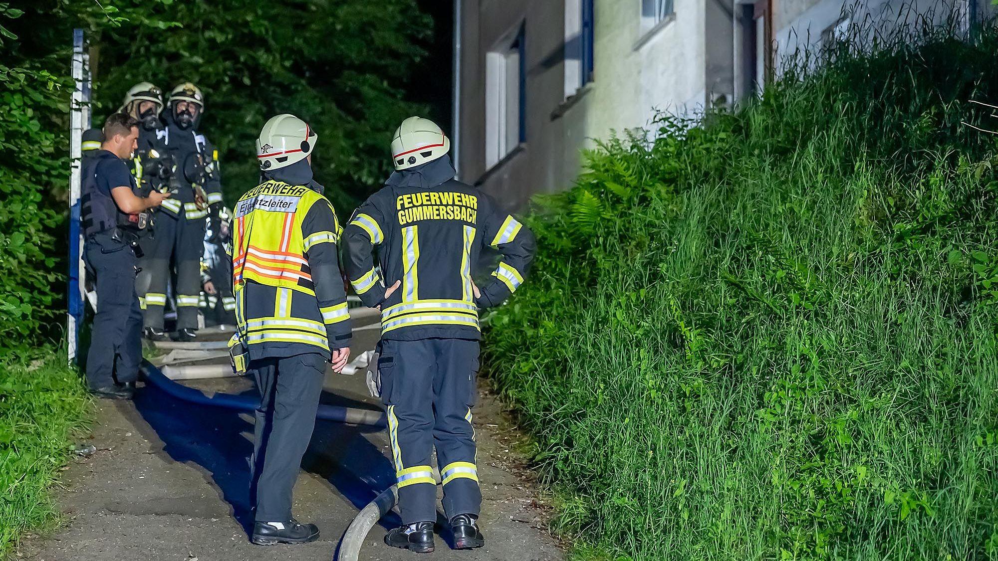 Mehrere Feuerwehrleute stehen vor einem Gebäude, in dem es gebrannt hat.