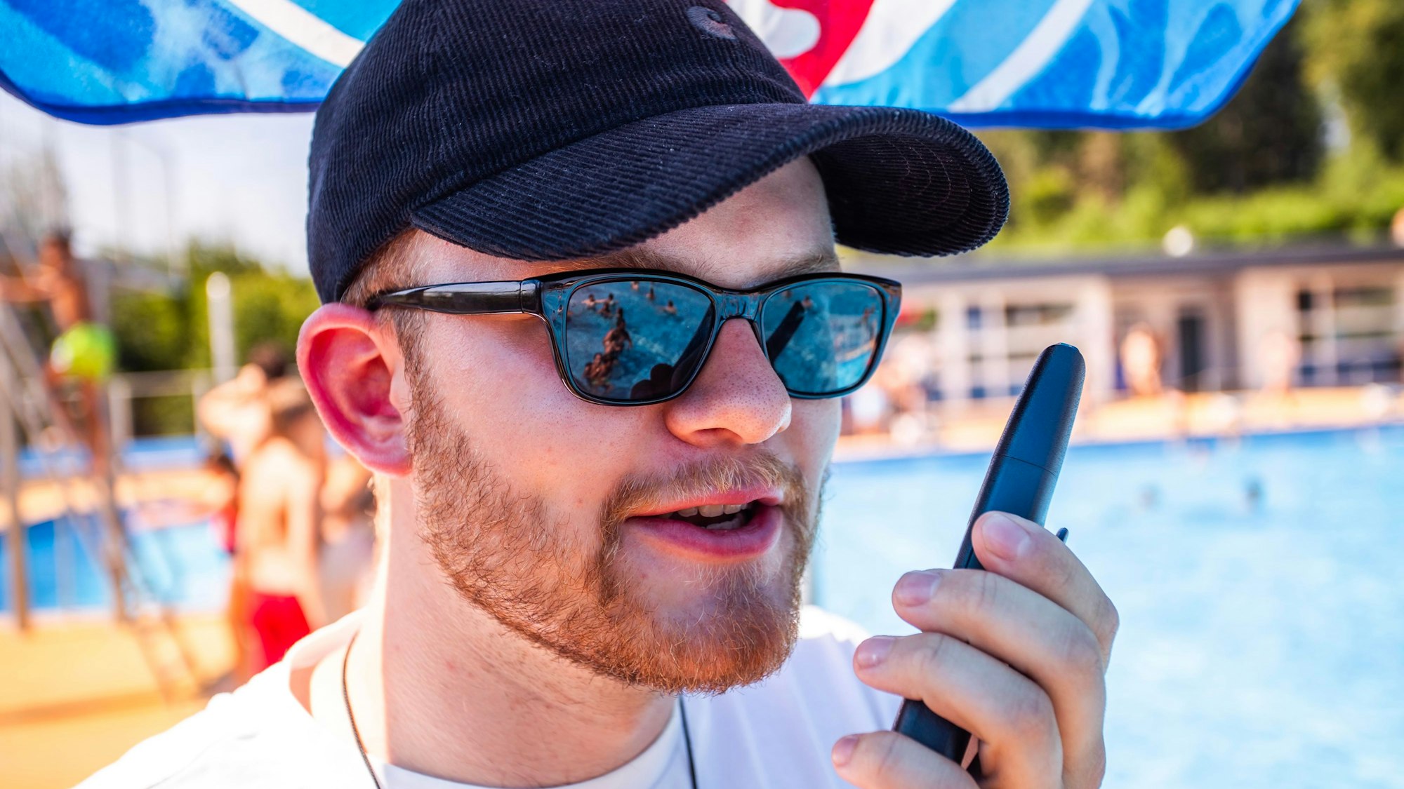 Ein junger Mann steht mit Walki-Talki am Beckenrand.