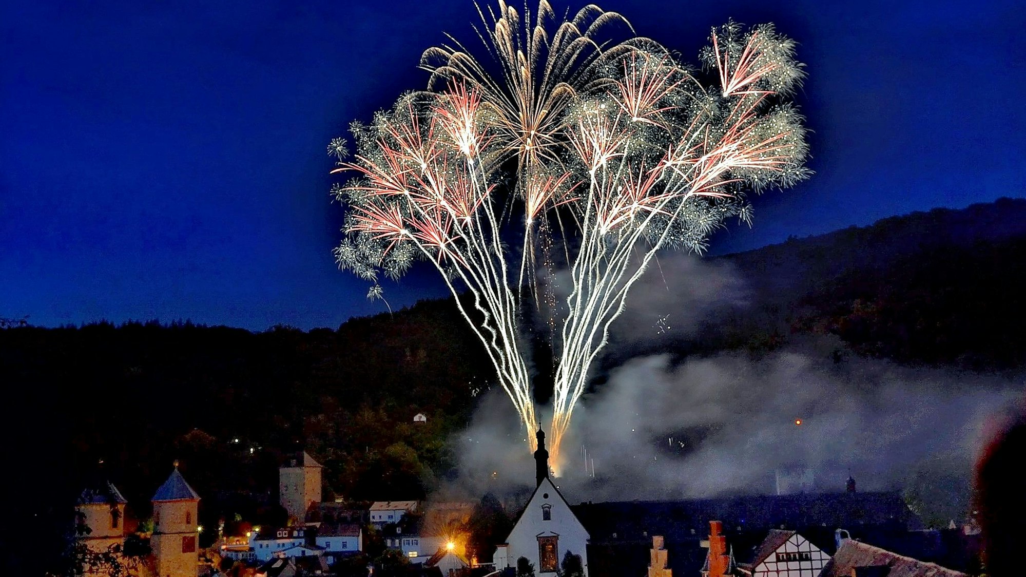 Ein Feuerwerk macht die Silhouette der Stadt Bad Münstereifel trotz Dunkelheit sichtbar.