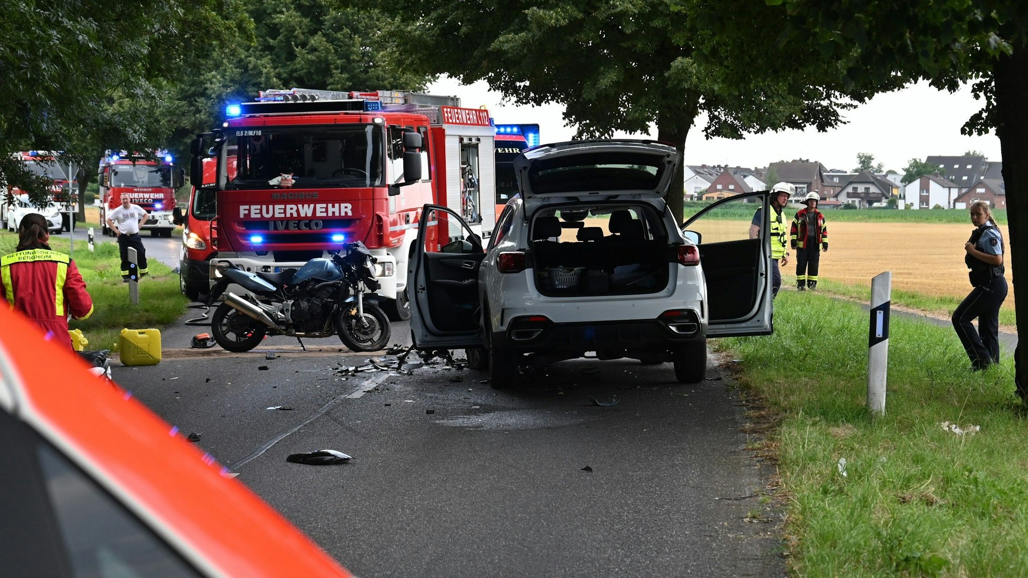 Das Bild zeigt die Unfallstelle. Ein Motorrad und ein Auto stehen auf der Straße, mehrere Einsatzkräfte stehen an der Unfallstelle.