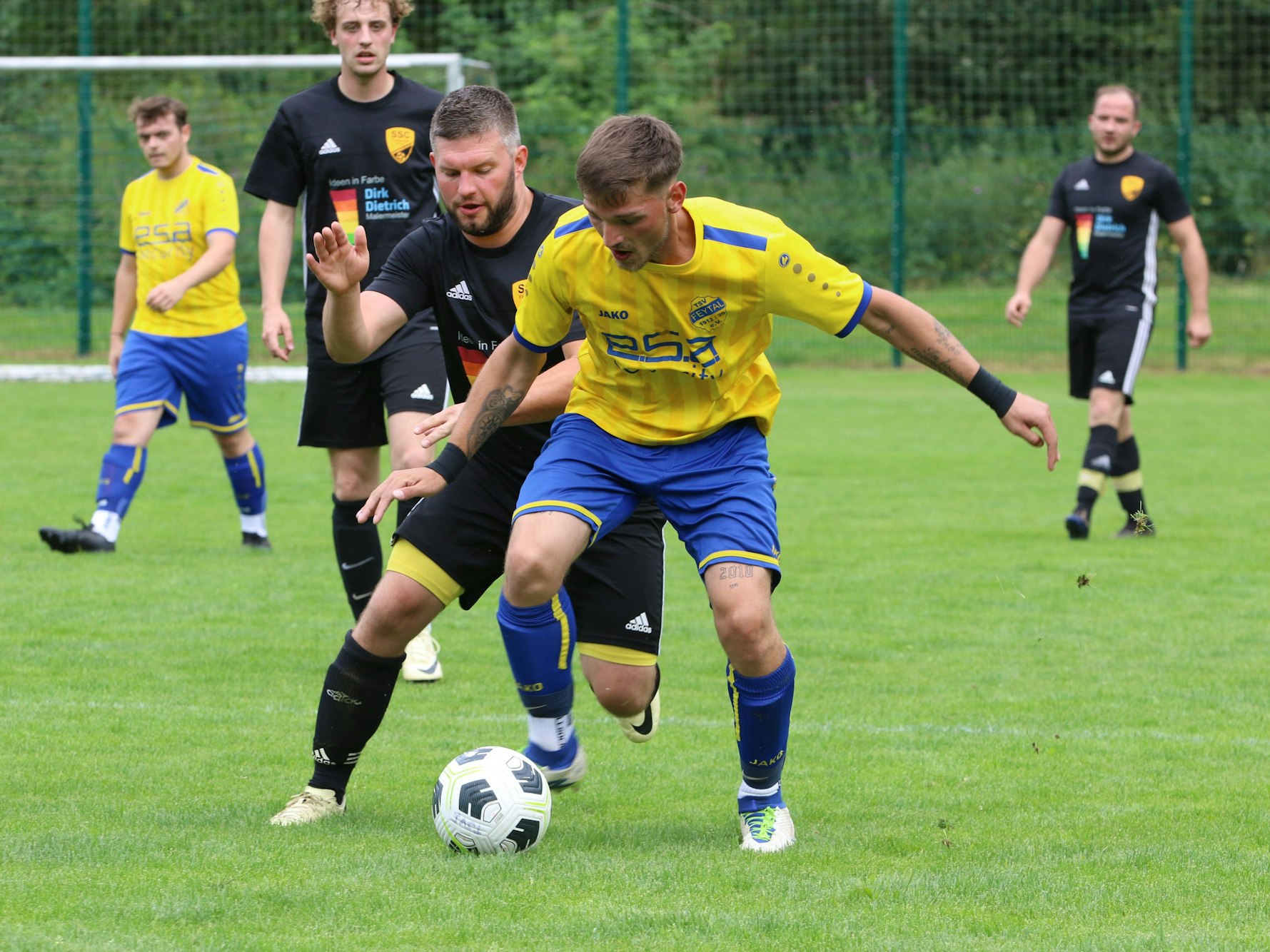 Ein Fußballer schirmt den Ball mit ausgebreiteten Armen vor einem Gegenspieler ab.