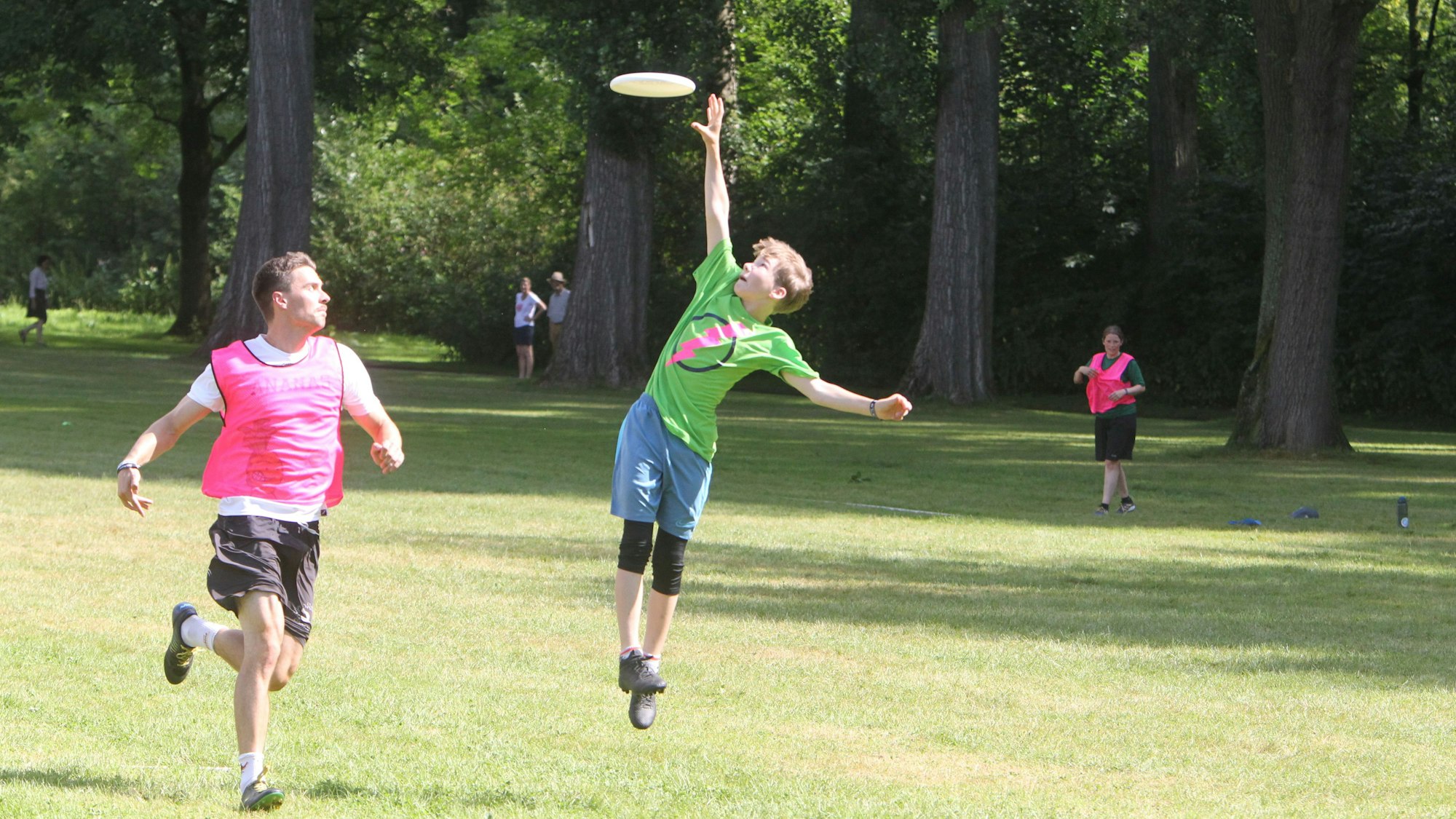 Ein junger Sportler springt hoch in die Luft, um eine herannahende Frisbee-Scheibe zu fangen.