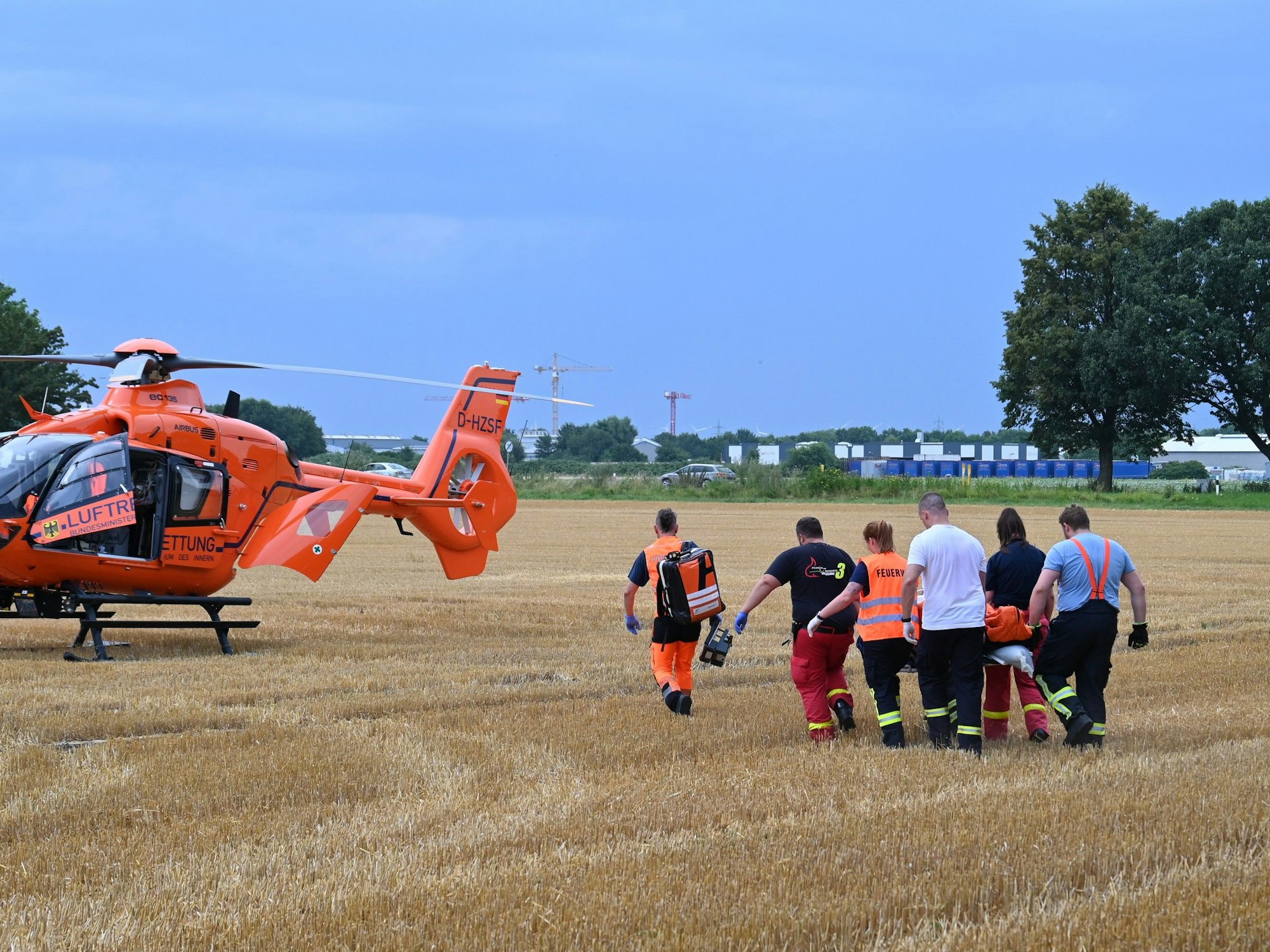 Das Bild zeigt mehrere Einsatzkräfte, die einen verletzten Mann auf einer Trage zum Rettungshubschrauber tragen.