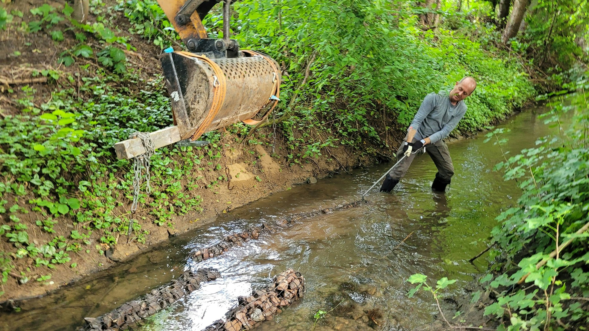 Ein Mann arbeitet in einem Bachbett, er bewegt eine Steinwalze.