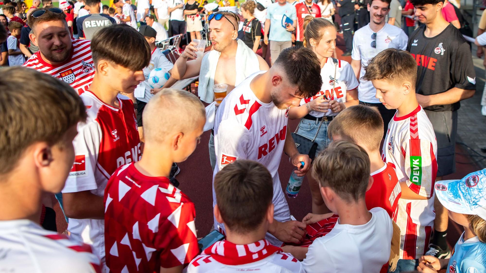Umringt von Fans in FC-Trikots schreibt Jan Thielmann Autogramme.