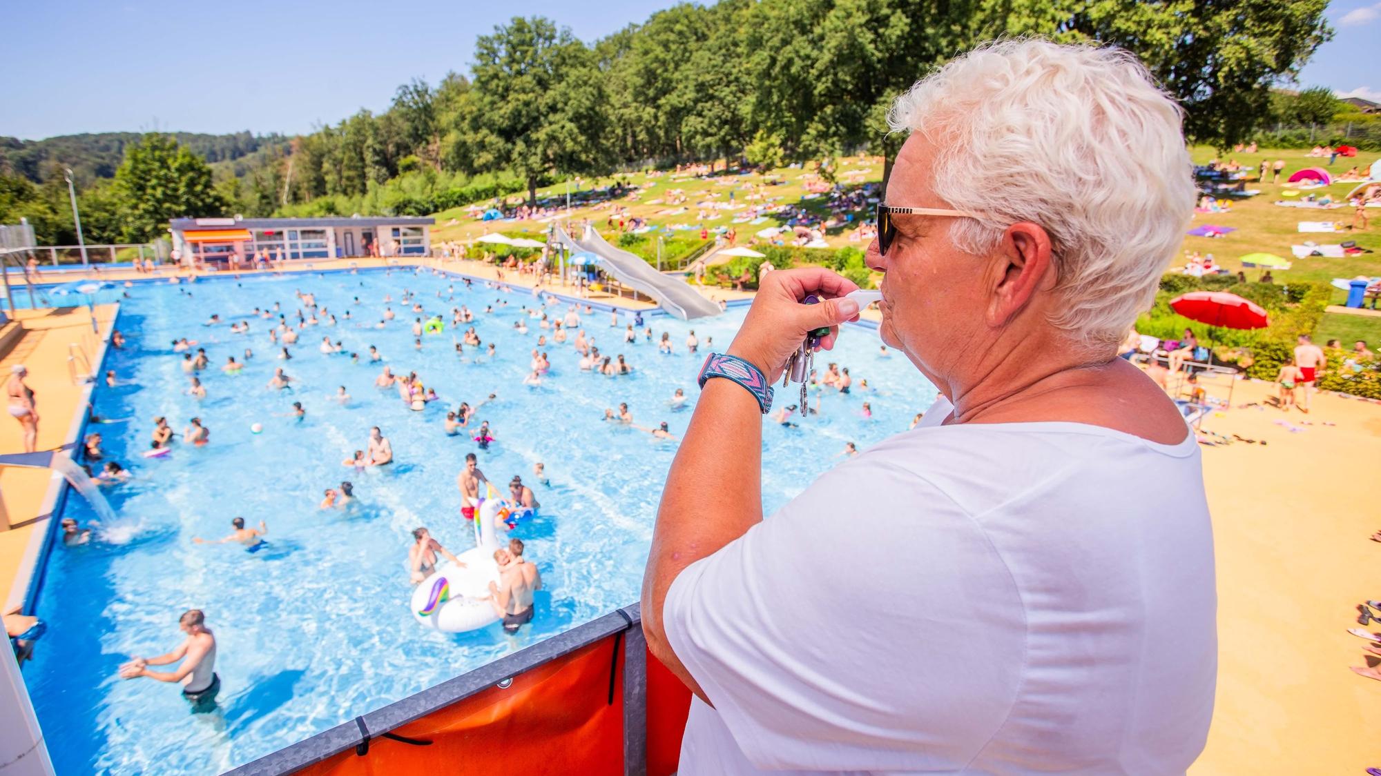 Eine Bademeisterin schaut von einem Aussichtspunkt aus auf ein Schwimmbecken und pfeift mit einer Trillerpfeife.