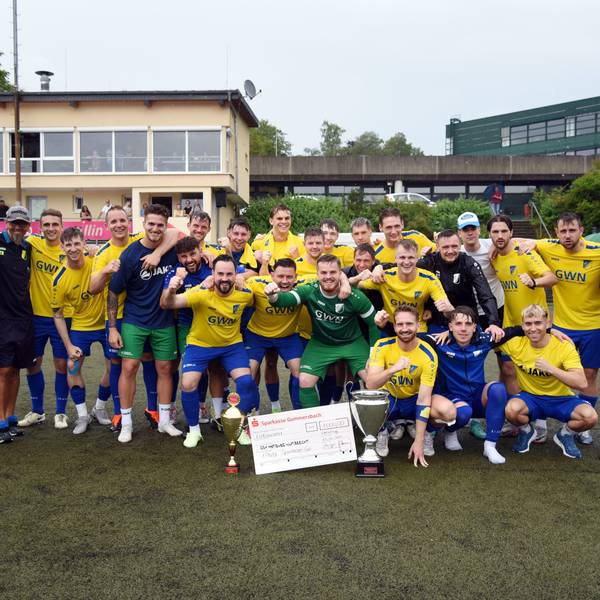 Die Landesliga-Fußballer des SSV Nümbrecht jubeln mit den Pokalen und dem Siegerscheck in die Karmera.