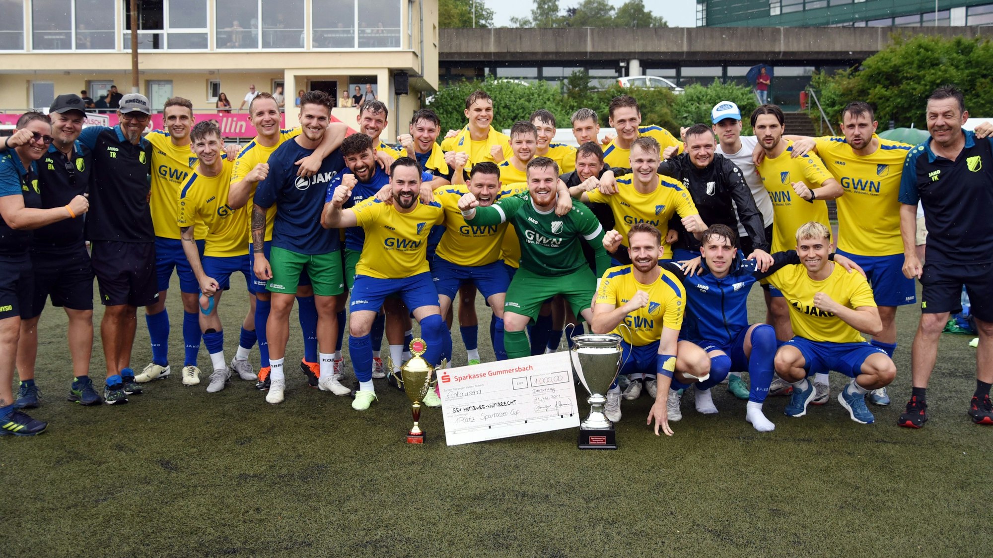 Die Landesliga-Fußballer des SSV Nümbrecht jubeln mit den Pokalen und dem Siegerscheck in die Karmera.