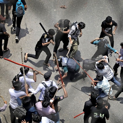 Studenten schlagen einen Polizisten mit Stöcken während eines Protestes gegen das Quotensystem im öffentlichen Dienst.