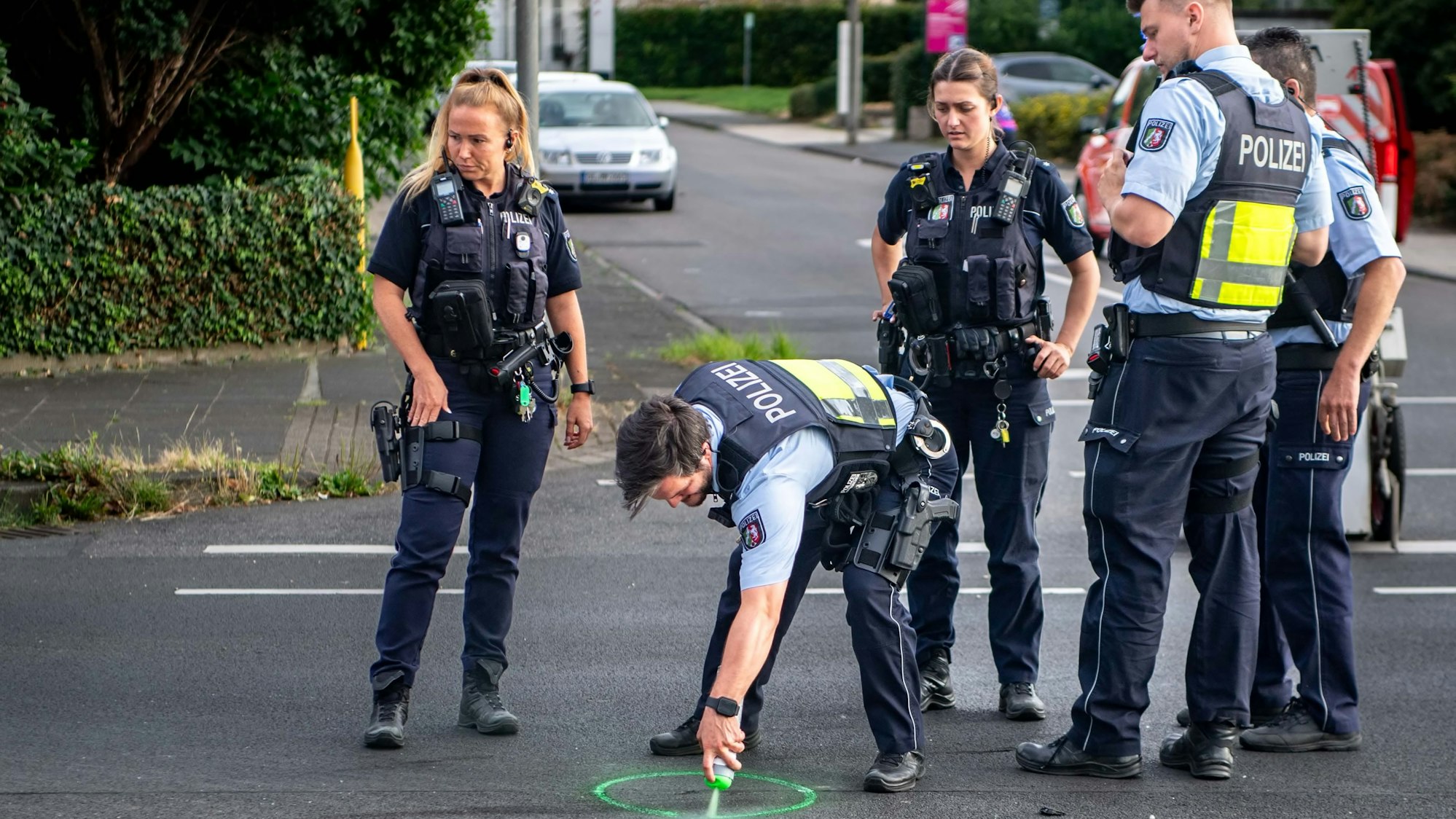 Das Bild zeigt fünf Polizisten an der Unfallstelle. Ein Beamter markiert mit grüner Sprühfarbe eine Spur.