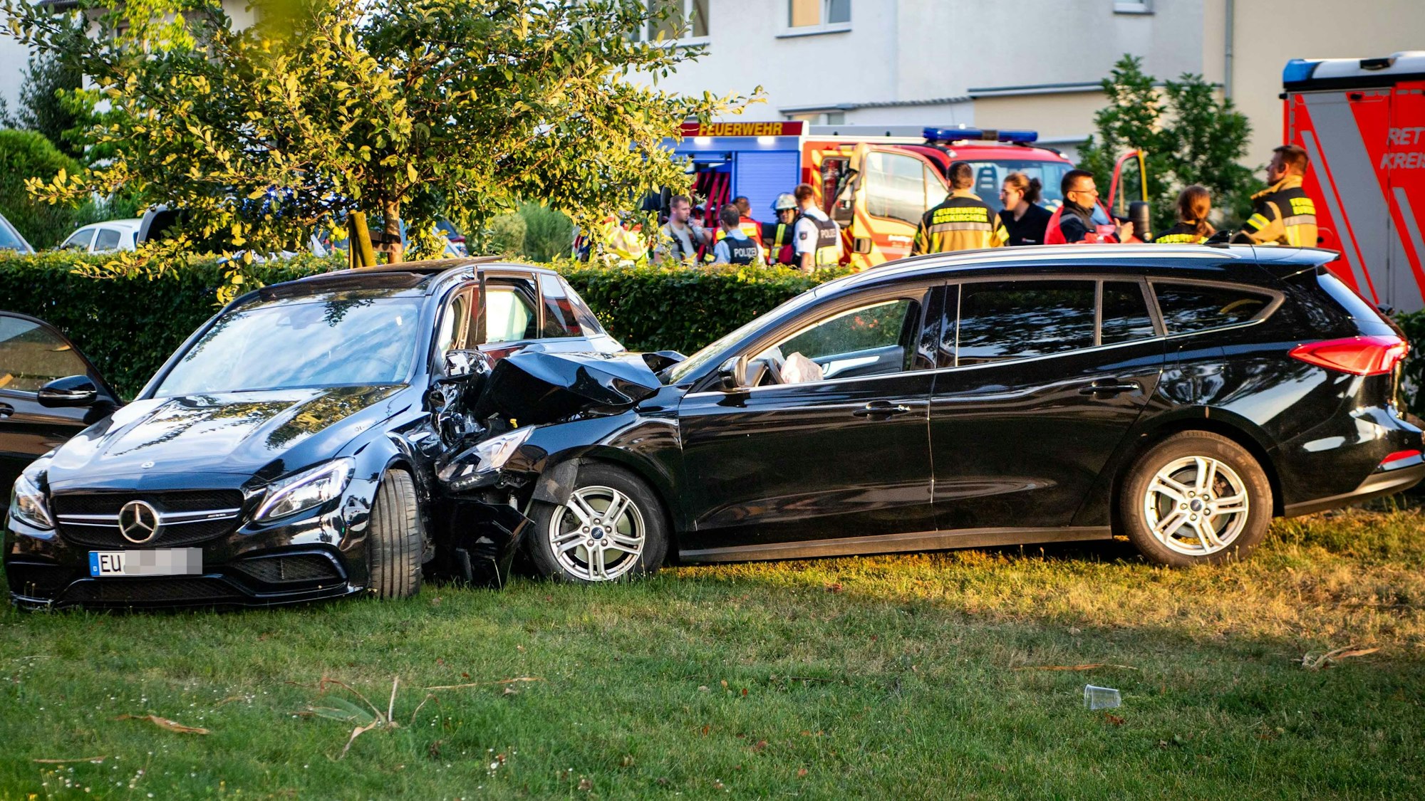 Ein schwarzes Auto ist in ein anderes schwarzes Auto gefahren. Beide Wagen stehen auf einer Wiese.