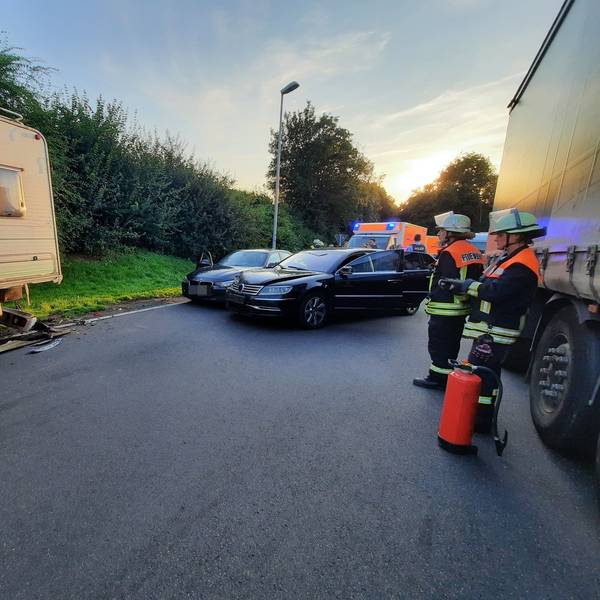 Drei Feuerwehrleute stehen in der Nähe von drei verbeulten Autos.