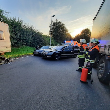 Drei Feuerwehrleute stehen in der Nähe von drei verbeulten Autos.