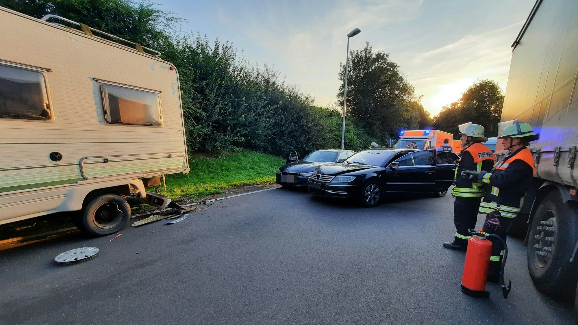 Drei Feuerwehrleute stehen in der Nähe von drei verbeulten Autos.