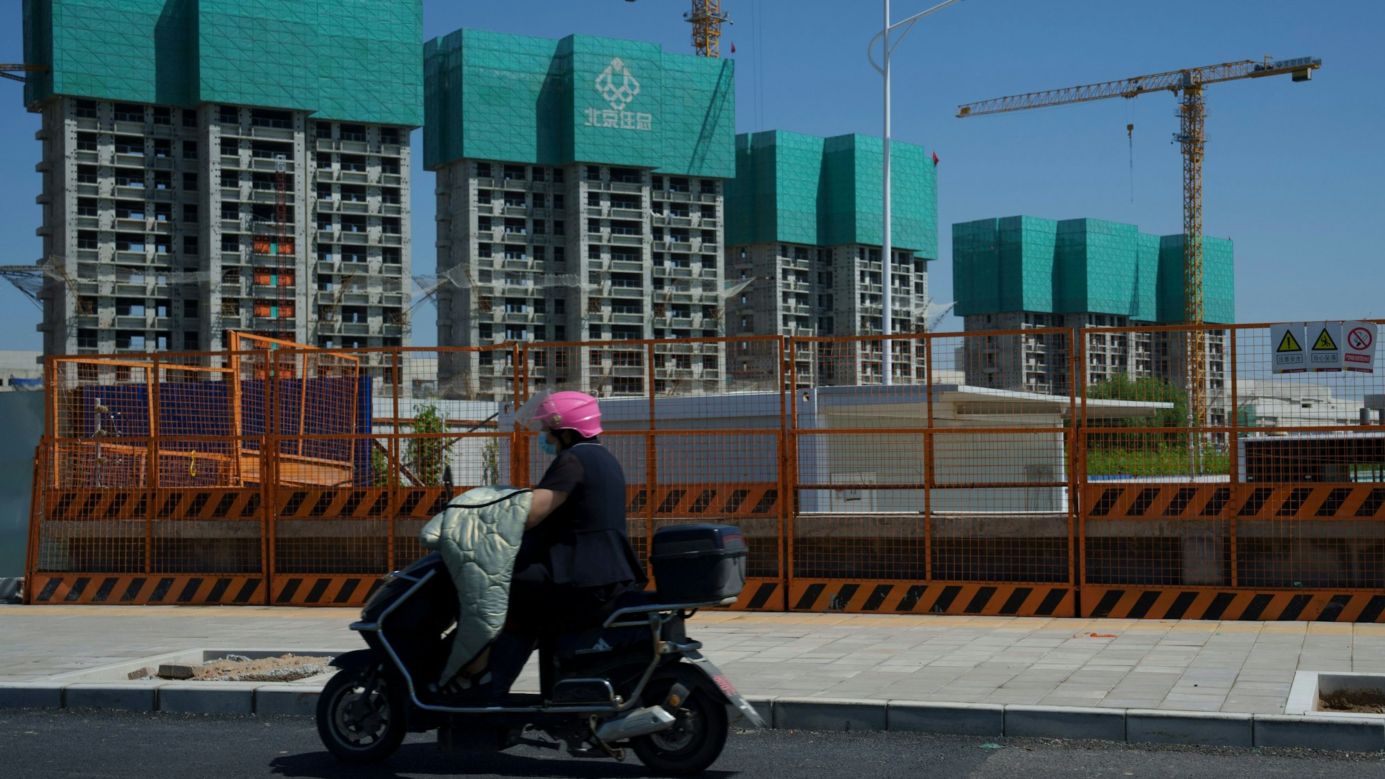 Eine Frau fährt an einem im Bau befindlichen Wohnprojekt am Stadtrand von Peking vorbei.