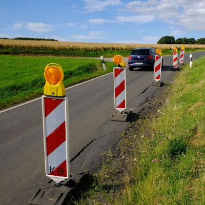 Am Rand der maroden Kreisstraße 58 zwischen Harzheim und Eiserfey stehen rot-weiße Warnbaken; ein Auto fährt vorbei.