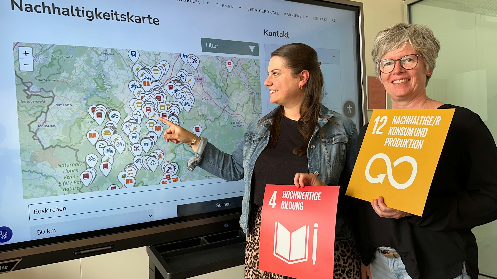Nachhaltigkeits-Koordinatorin Lisa Rodermann und Abfallberaterin Karen Beuke stehen vor einem Bildschirm, auf dem die Nachhaltigkeitskarte zu sehen ist.