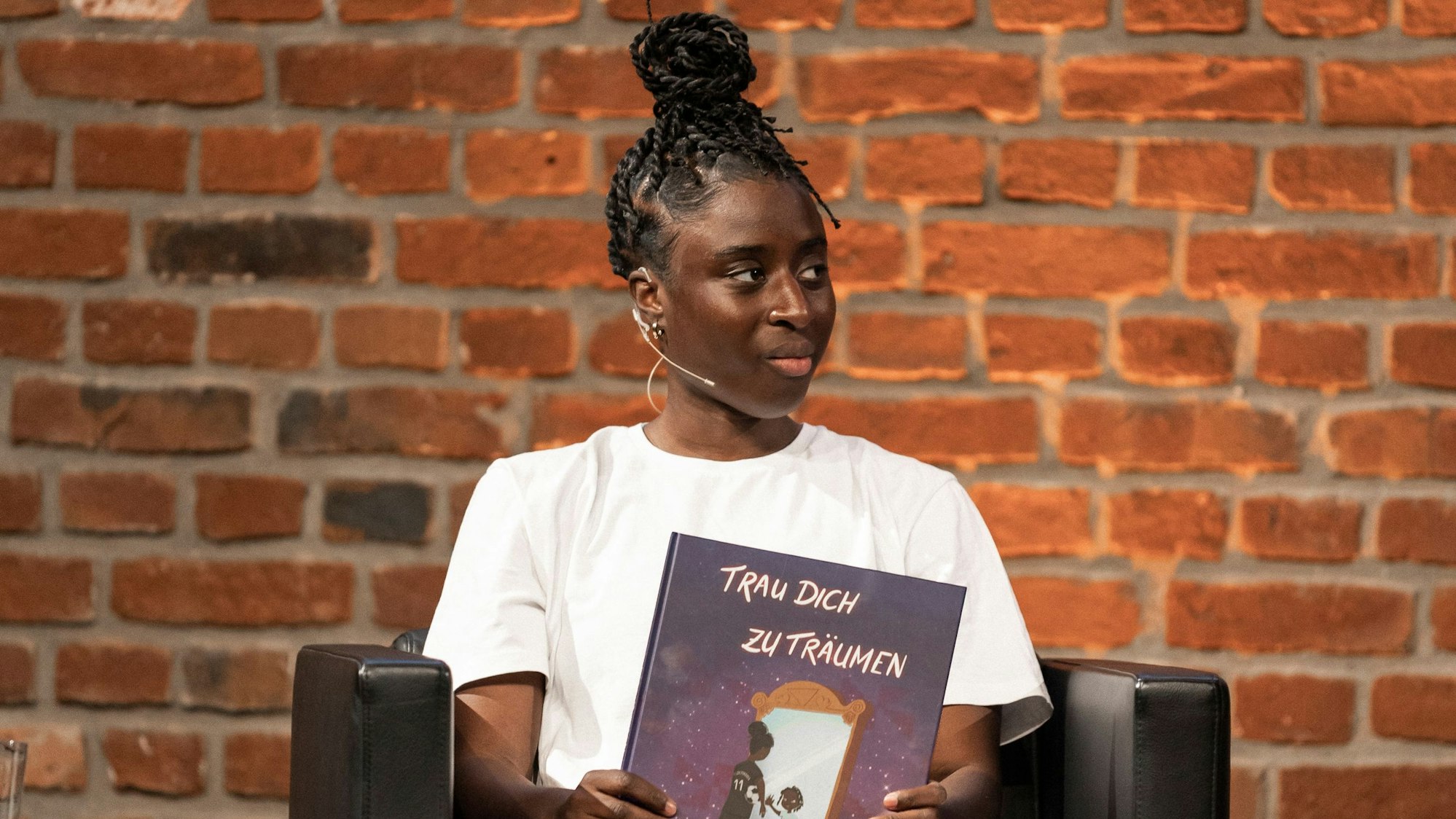 Fußballerin Eunice Beckmann sitzt mit dem Buch „Trau dich zu Träumen“ auf einem Sessel