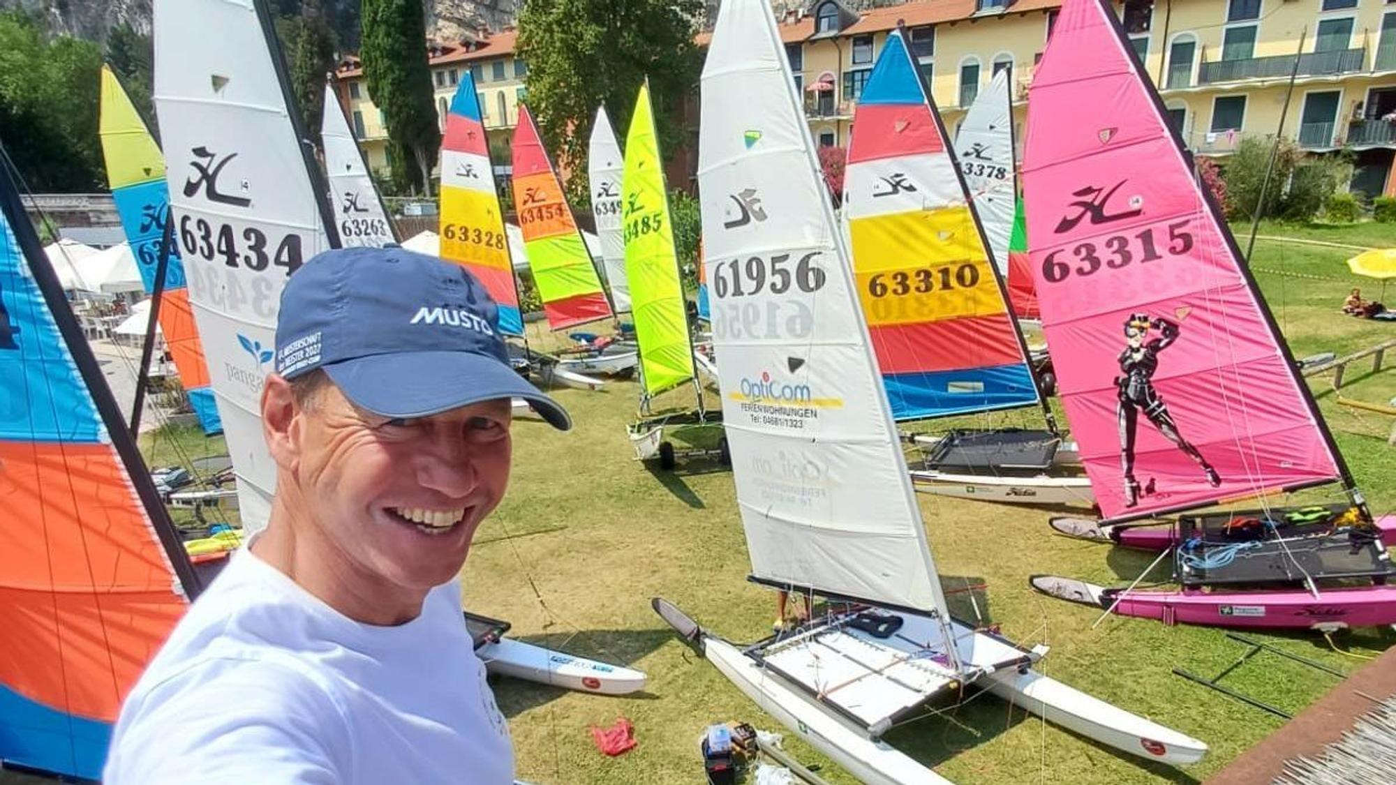 André Hauschke strahlt über das ganze Gesicht. Im Hintergrund zahlreiche Segelboote auf einer Wiese.