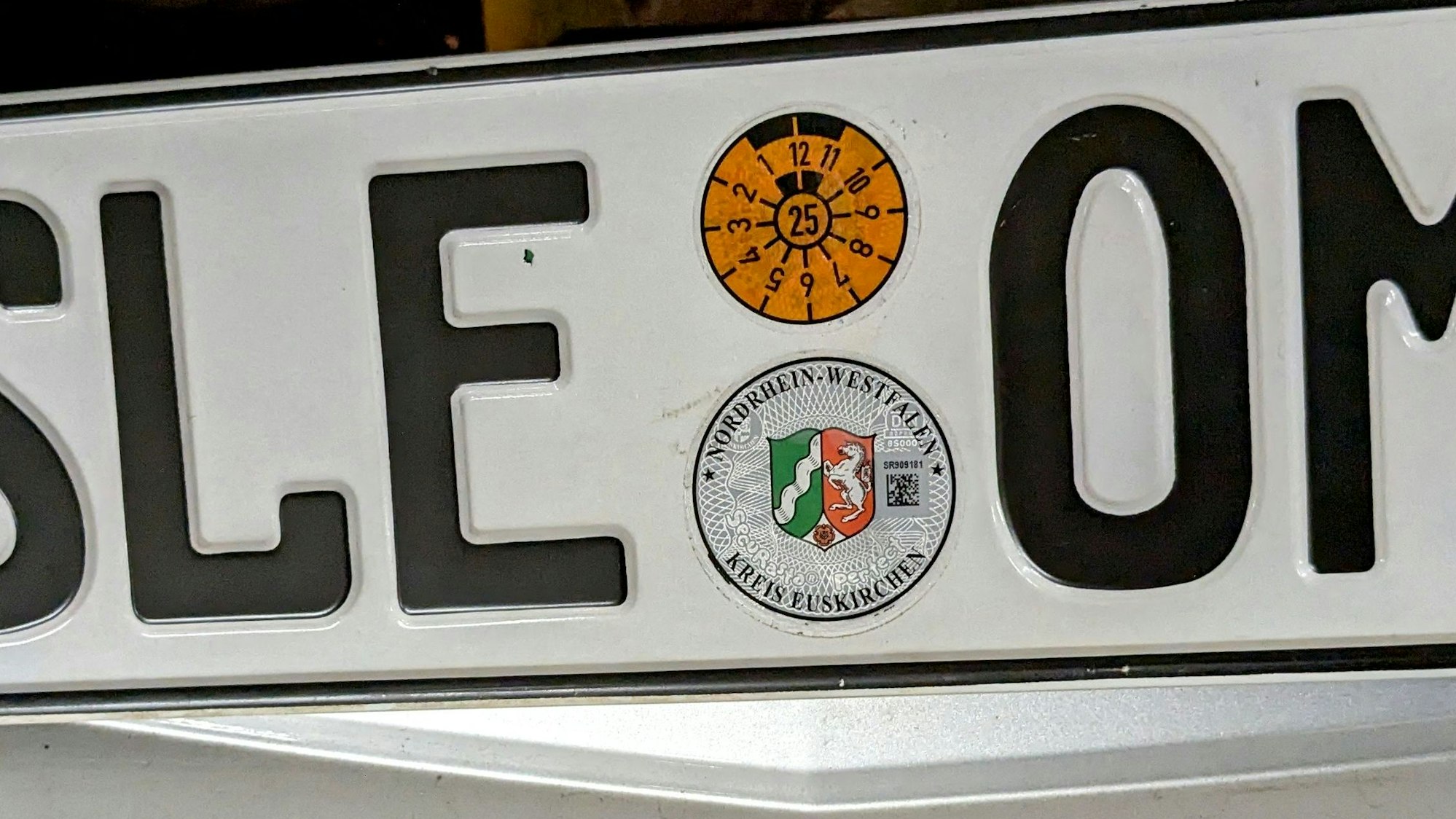 Ein Autokennzeichen mit der Kennung SLE, HU-Plakette und Siegel des Kreises Euskirchen.
