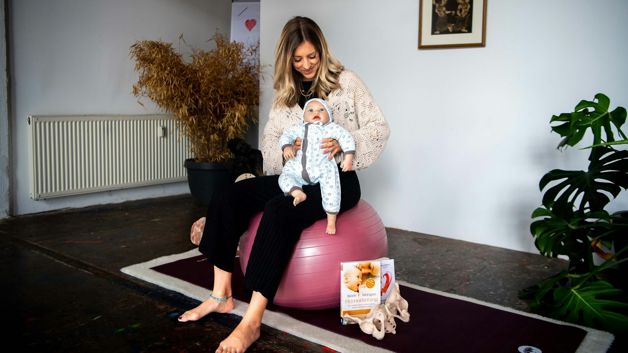 Das Bild zeigt Kerstin Blindert, auf einem Ball sitzend. Sie hat eine Puppe im Arm.