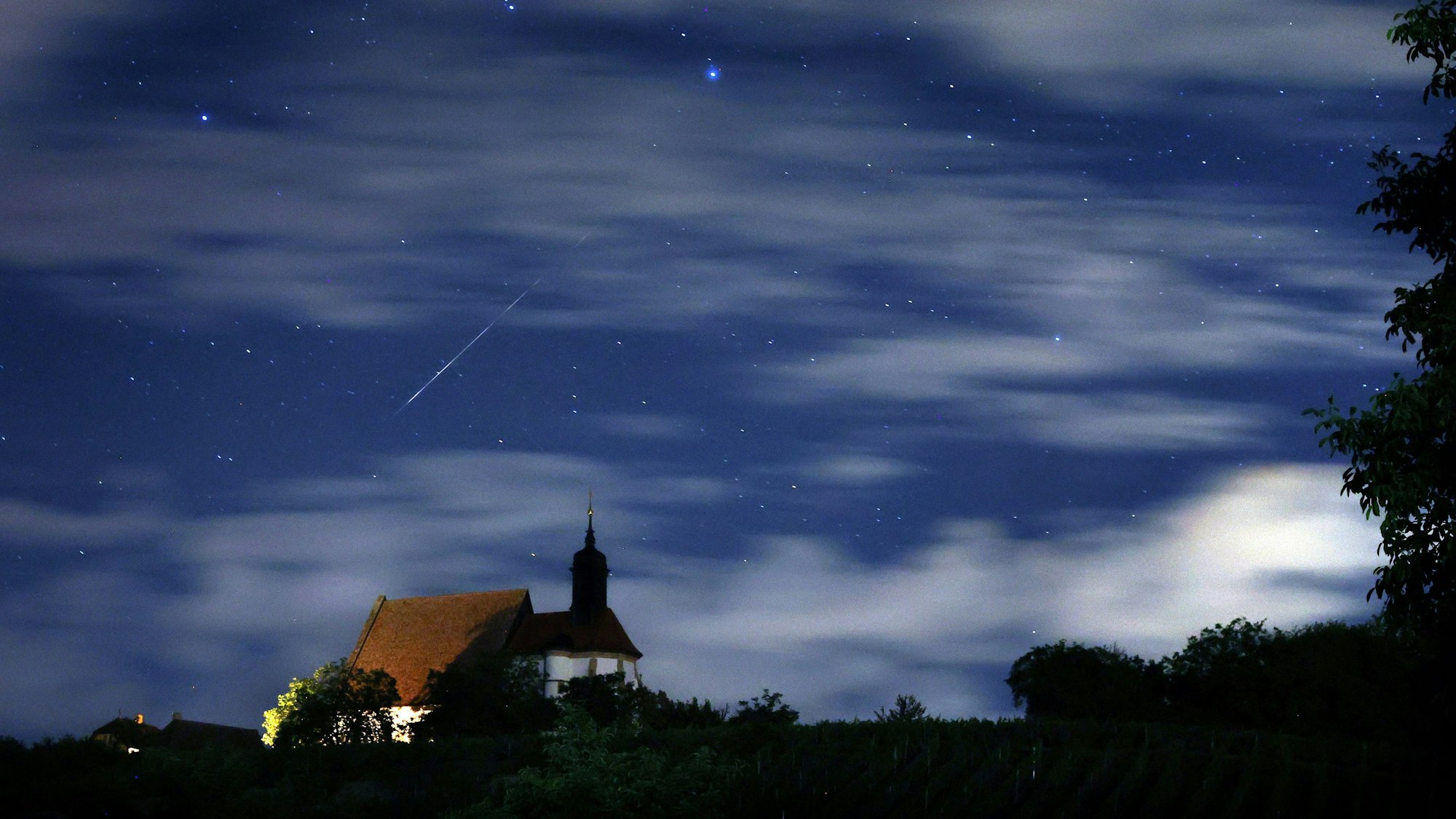 ARCHIV - 13.08.2023, Bayern, Volkach: Eine Sternschnuppe verglüht am Himmel über der Wallfahrtskirche Maria im Weingarten.