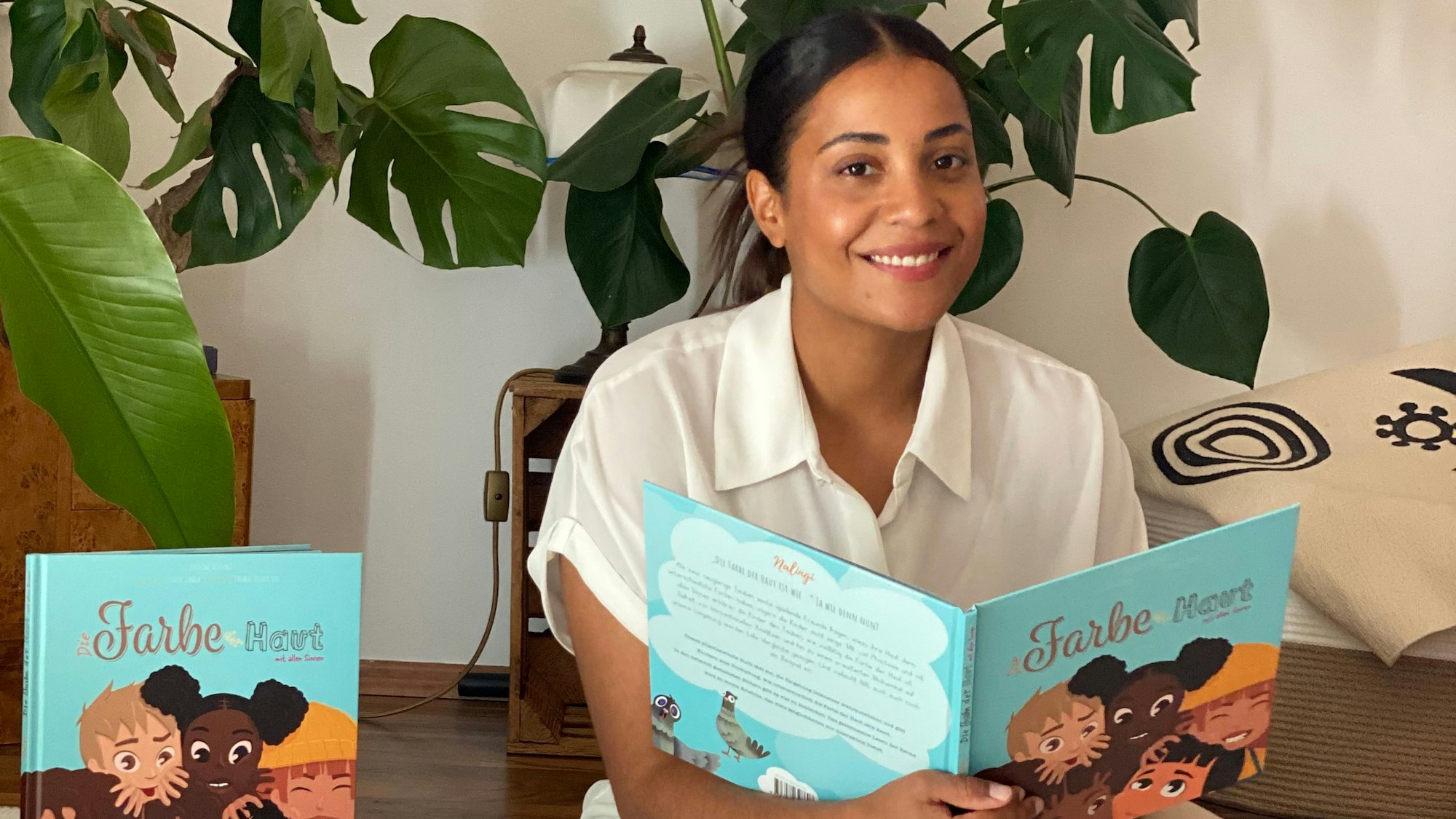 Joceline Altevogt sitzt lächelnd mit ihrem Buch „Die Farbe der Haut mit allen Sinnen“ auf dem Boden.